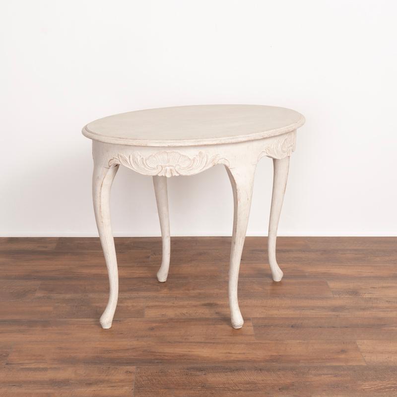 This oval shaped side table from Sweden is simply charming with it's softly rounded edges, decorative carved details and cabriolet legs. There is a gentle appeal in the newly professionally applied antique white paint that has been lightly scraped