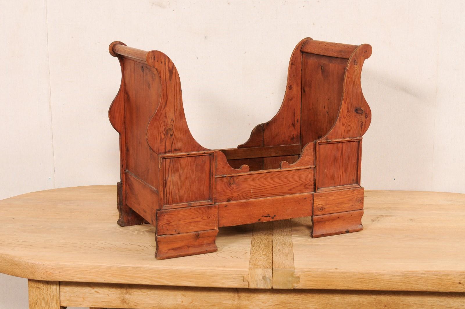 A Swedish carved-wood dog bed from the early 20th century. This antique dog bed from Sweden has a wonderful sleigh bed design, with exaggerated head and foot posts raising up into lovely scrolled volutes. The sides are nicely appointed with carved