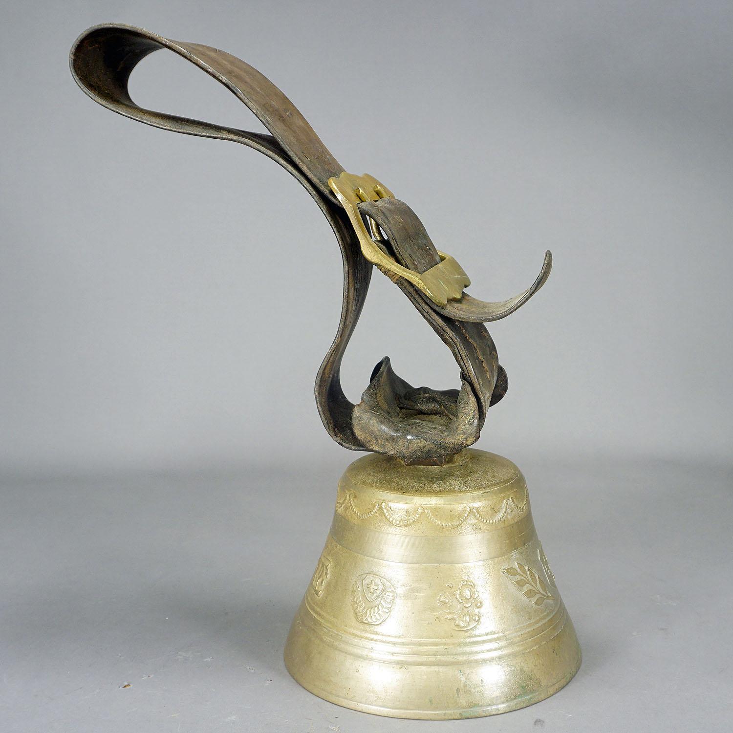 A large casted bronze cow bell from the alps region of Switzerland, manufactured around 1900. The antique bell features high relief motifs of heraldig symbols of Swizerland and edelweiss as well as a foundy mark. The bell comes with its original