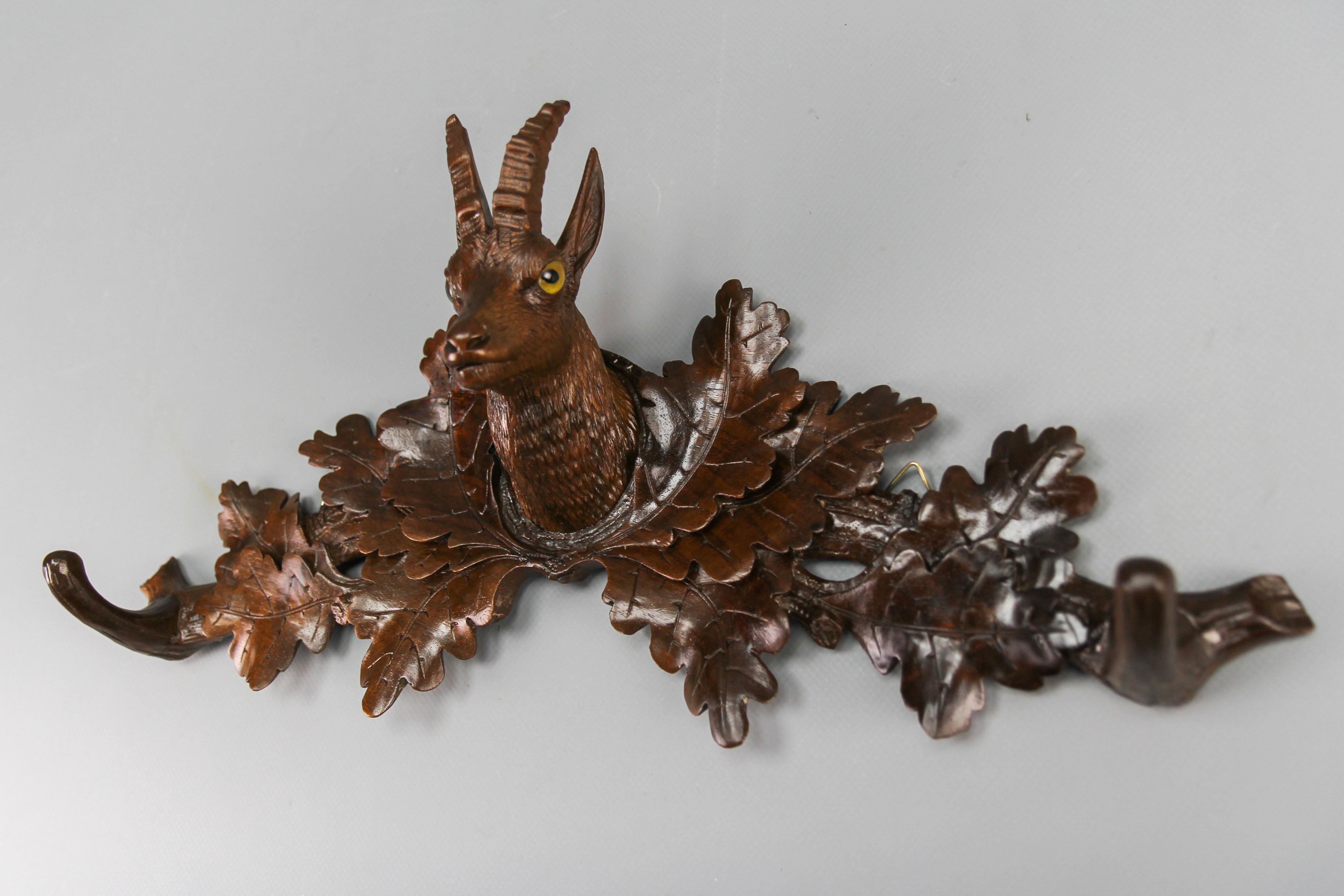 Swiss Black Forest coat rack or hat rack with chamois head and carved oak leaves, made of walnut, late 19th Century.
This antique wall-hanging coat rack features a beautifully hand-carved chamois head with glass eyes, placed at the center of the