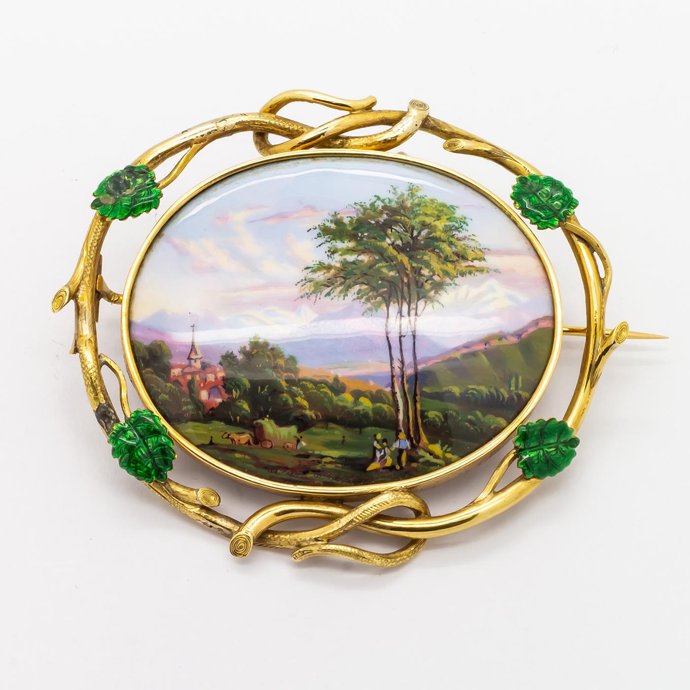 A Swiss enamel brooch, with an oval hand painted scene depicting mountains in the distance with a church surrounded by trees, with a feature tree, people and animals to the foreground, within a twisted gold frame with four green enamel leaves, circa