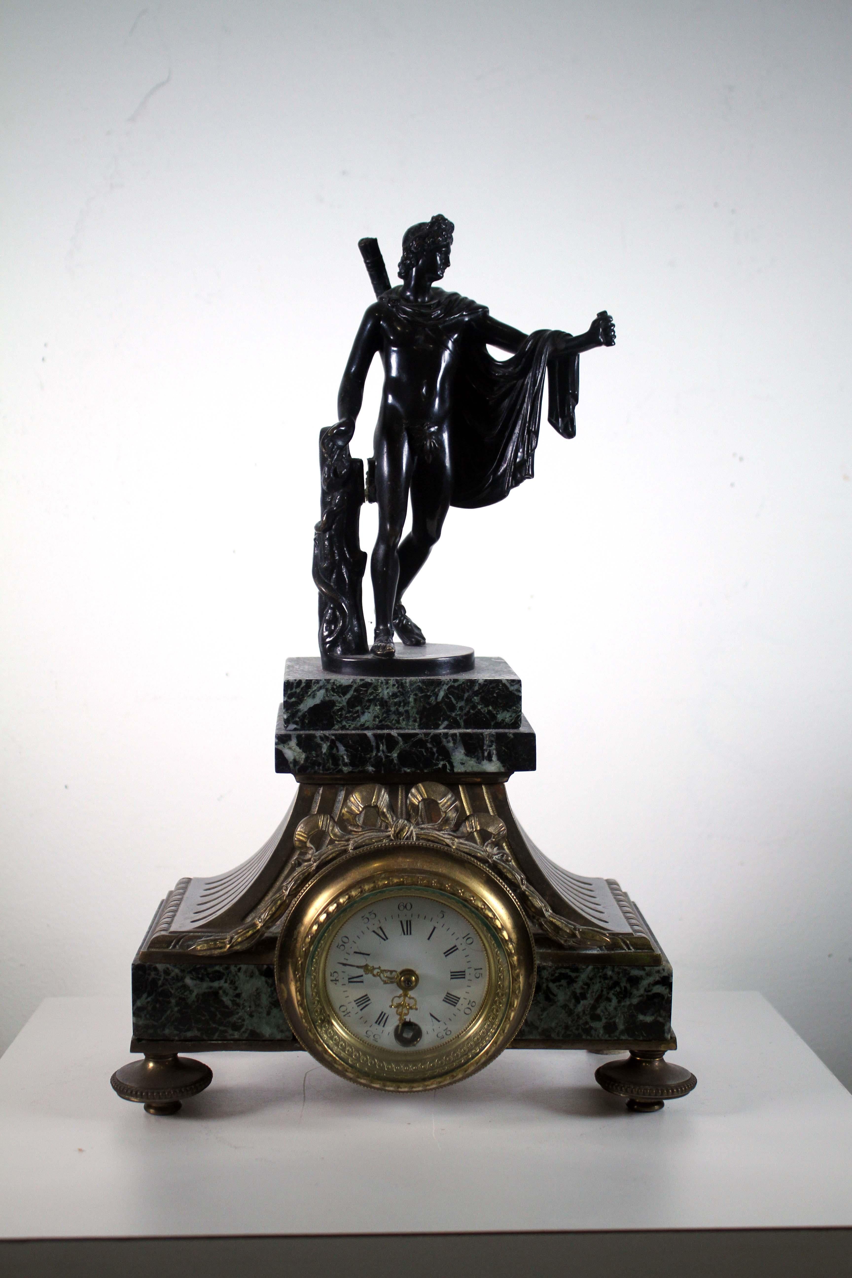 This is a stunning antique Swiss Lenzkirich clock. It features a beautiful iron bronze case with an Apollo figure atop the dial. The clock face is adorned with delicate black Roman numerals and a pair of finely crafted hands. The intricate details