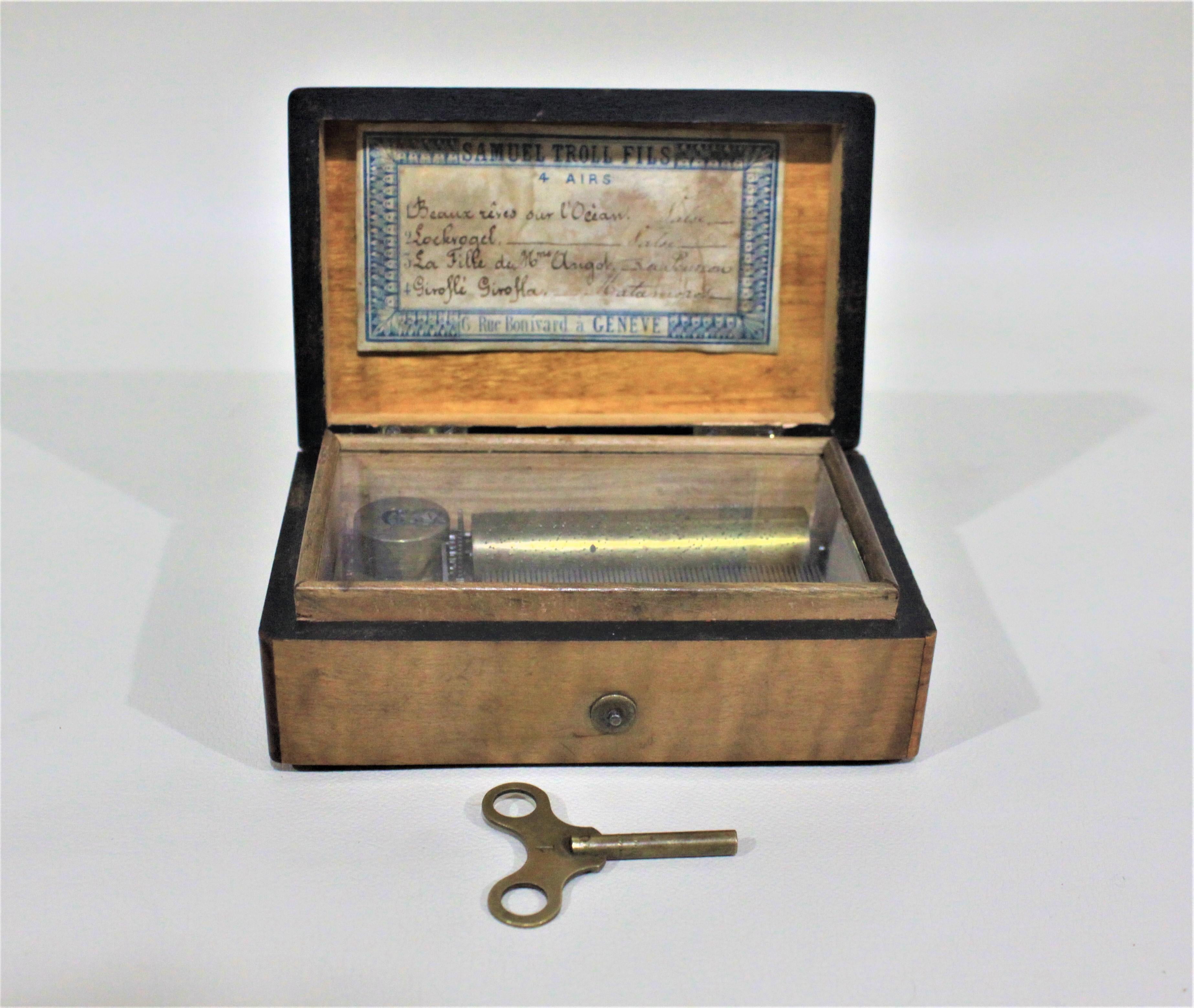 Fabriquée en Suisse vers 1850, cette boîte à musique à cylindre en laiton à remontage par clé est placée dans un coffret en noyer ronce avec un écusson incrusté sur le dessus et un couvercle de protection en verre sur le mécanisme. L'intérieur du