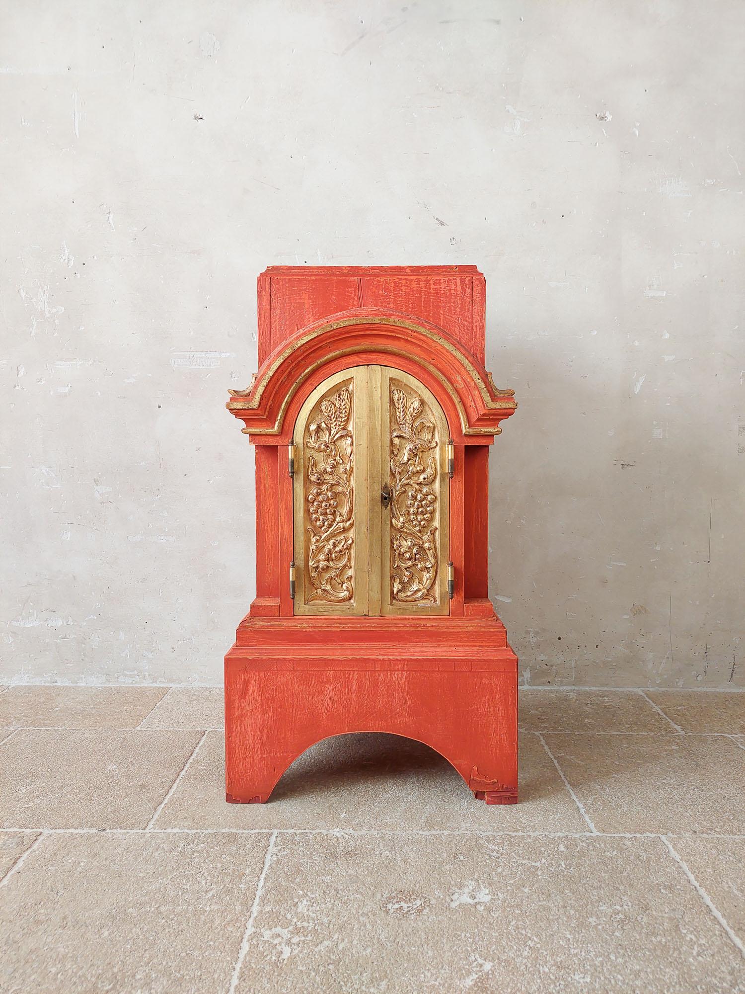 Antique table altar or tabernacle, patinated in orange terra color with golden doors.

h 95 x w 50 x d 47 cm