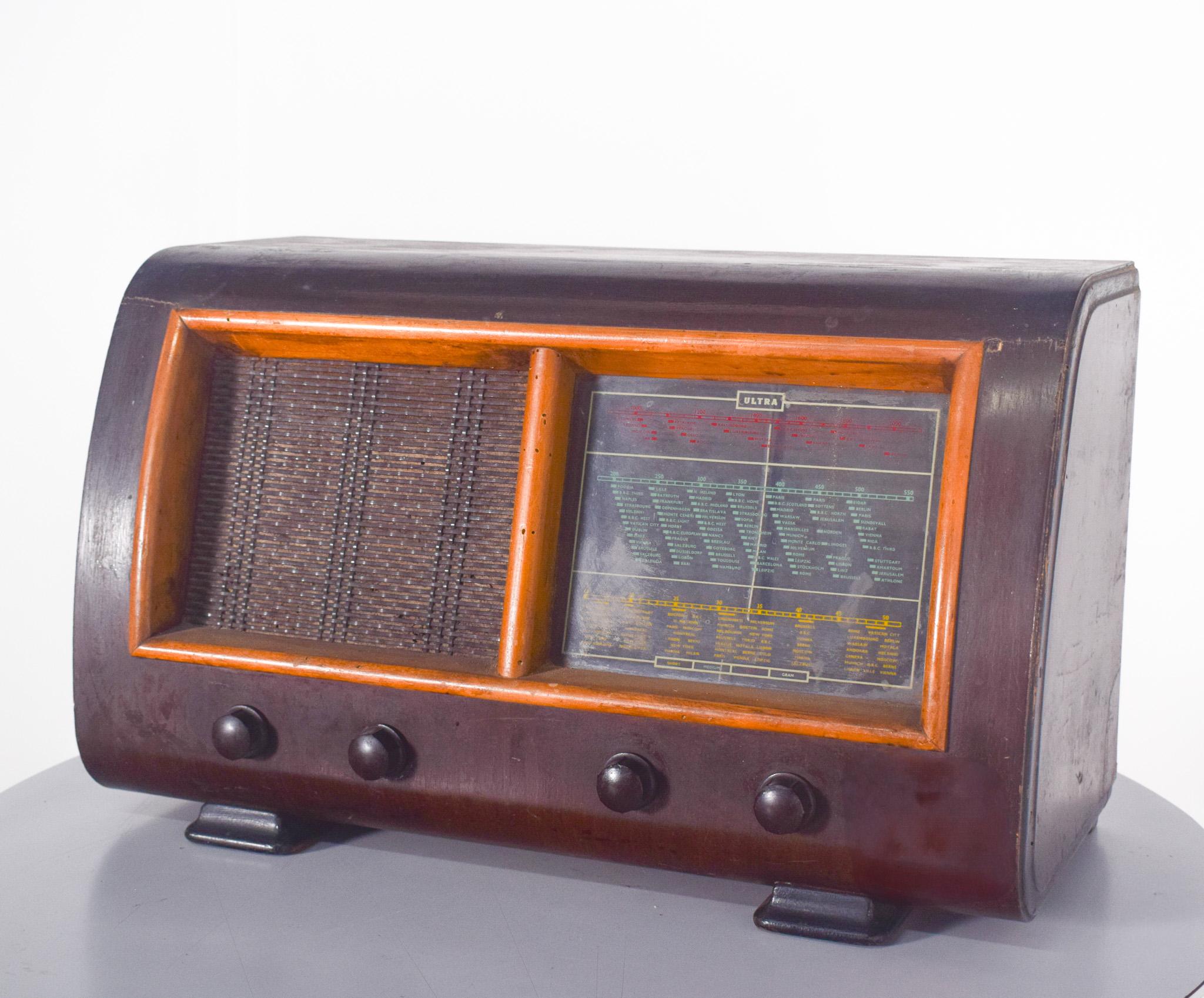 Radio de table ancienne avec coffret en bois.  Avec un design classique, probablement des années 40 et 50, et une structure robuste en bois foncé.
La grille du haut-parleur est recouverte d'un tissu, permettant au son de sortir avec une bonne
