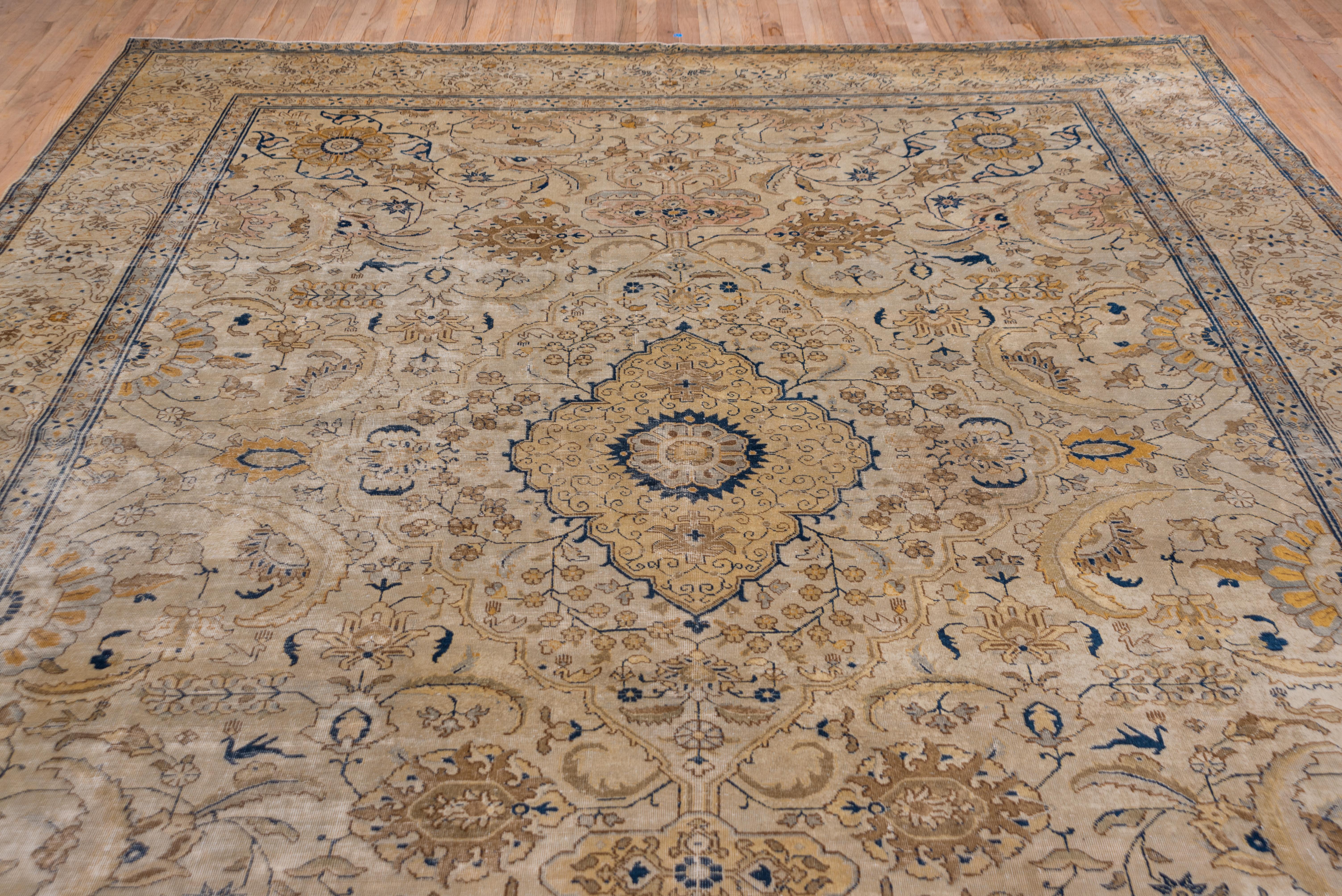 The sand ground of this well-woven NW Persian city carpet shows a small scalloped straw medallion set within a pattern of large sickle leaves, petal rosettes, ragged palmettes and flowering sprays and vines. The sand/straw border features a strong