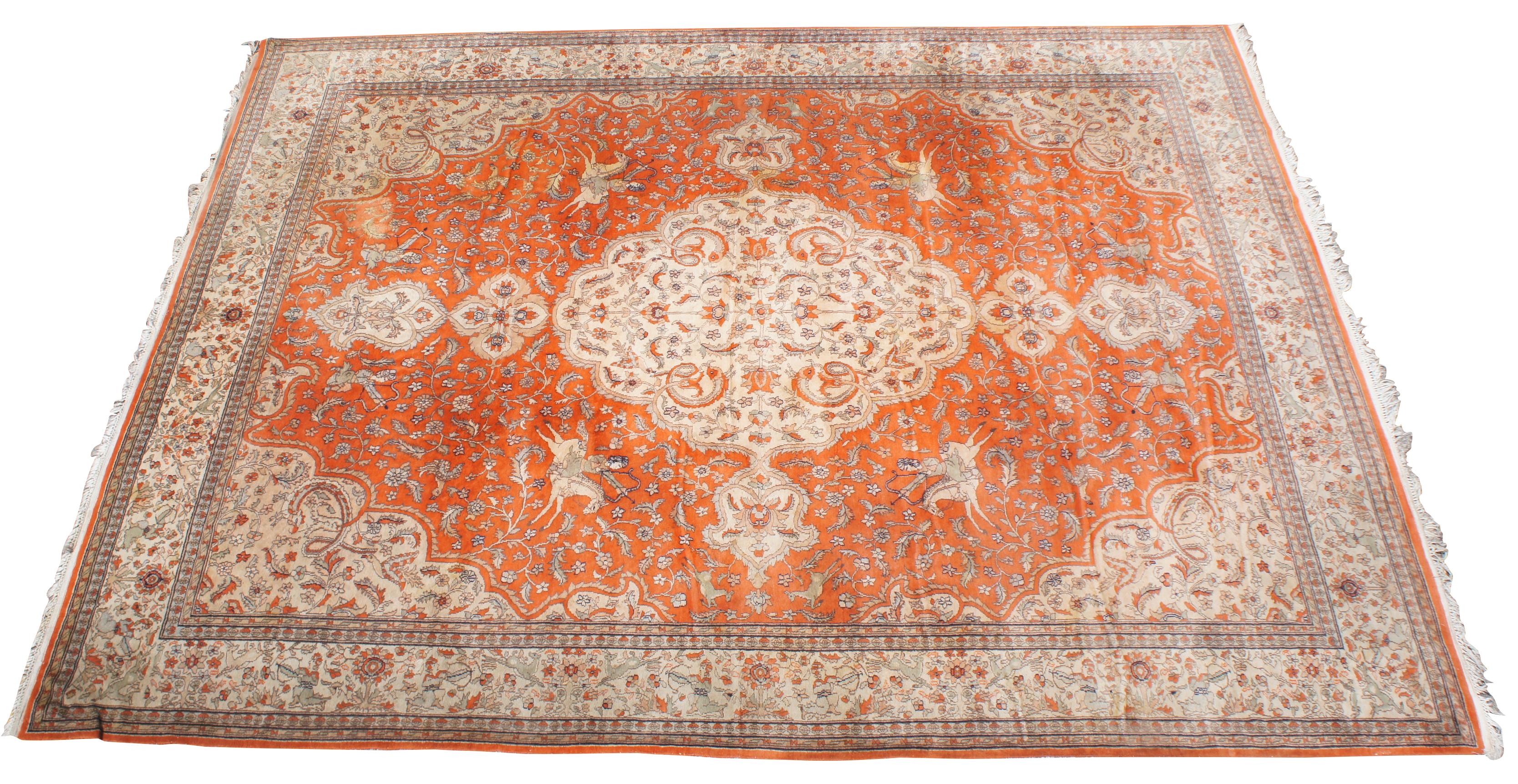 Antique hand knotted Tabriz Indo Persian area rug with a hunting scene on an orange field or forest. Features hunters shooting antelope or deer with arrows on horses and by foot. The center medallion and boarder features cream or tan floral motifs,