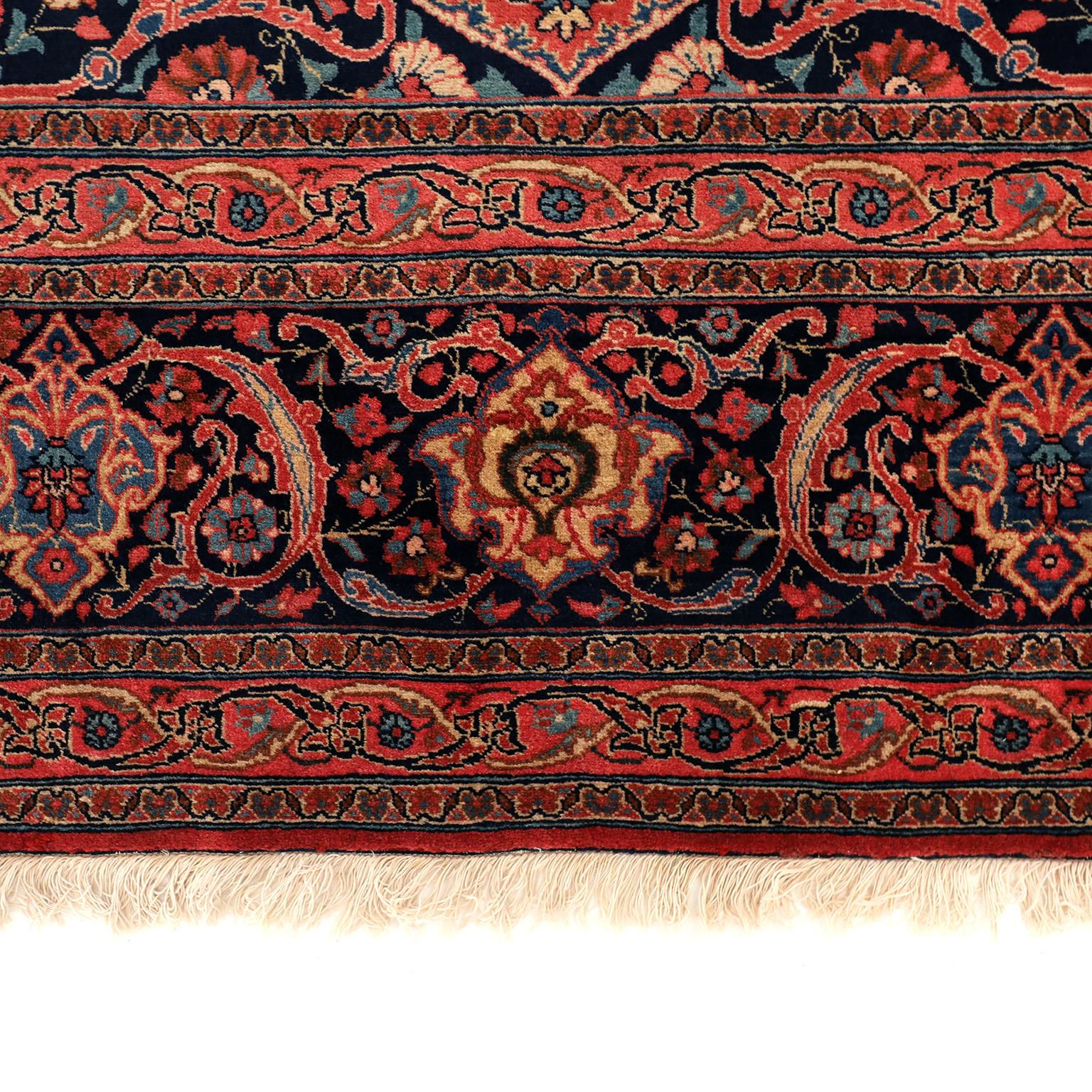 This antique Persian carpet in red and indigo circa 1920 measures 11' x 15' and consists of a handspun hand knotted wool pile and organic vegetable dyes. The shades of red vary throughout the central medallion, field, and border, as the natural