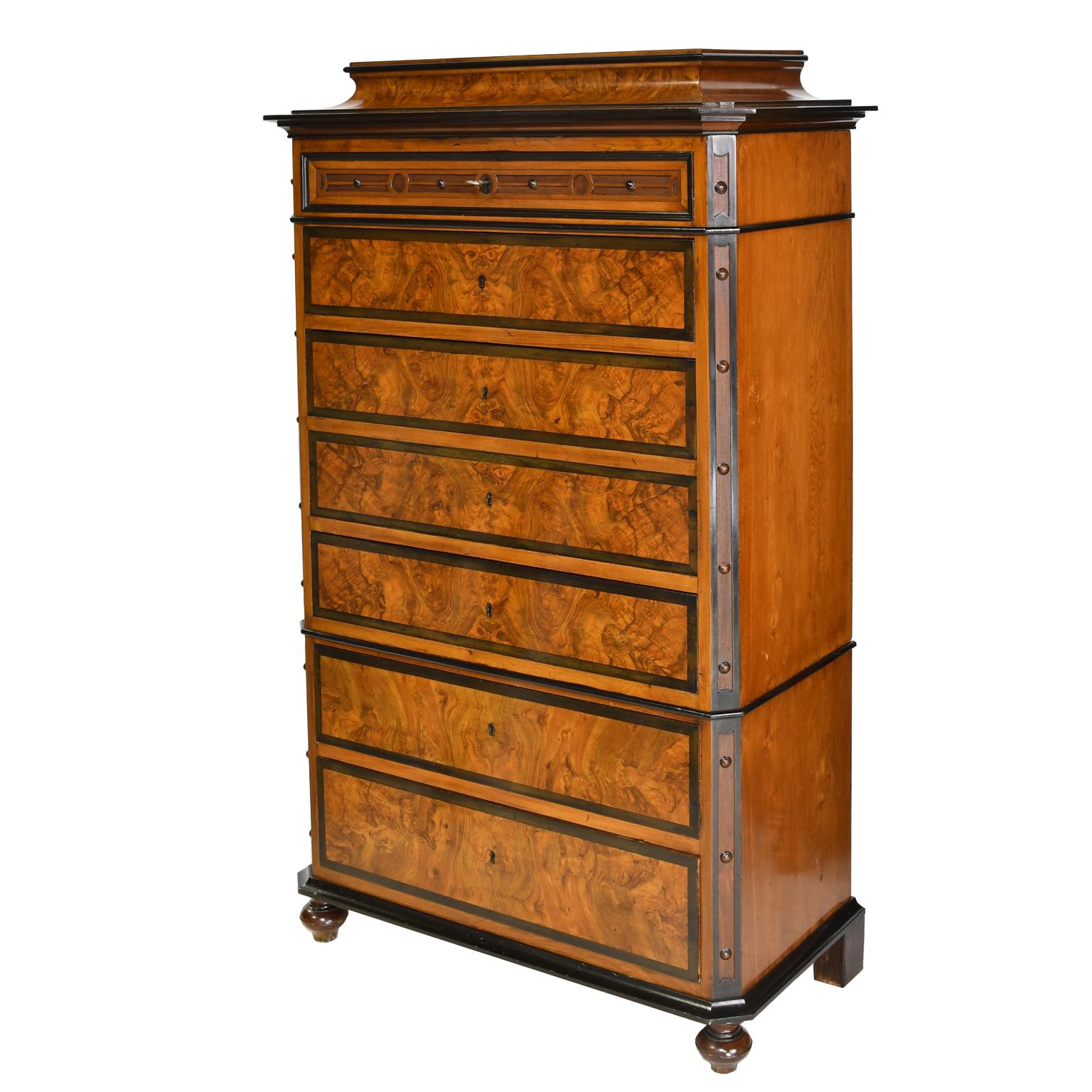 A handsome tall chest on chest in beautiful burled walnut with ebonized accents. Offers seven drawers of variegated heights with  their original working locks and one key, original turned feet, and a distinctive pedestal top. Drawers operate