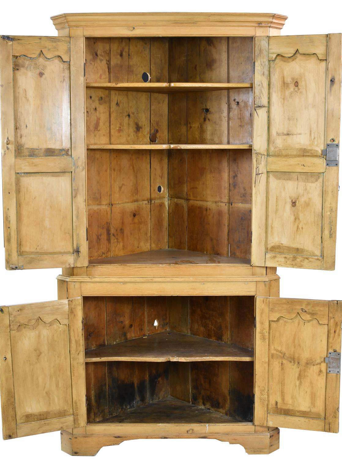 Charmante armoire d'angle de style anglais en pin clair de couleur miel avec des coins chanfreinés, quatre portes avec des panneaux encastrés et une moulure supérieure festonnée et sculptée, et reposant sur des pieds en forme d'équerre. L'intérieur