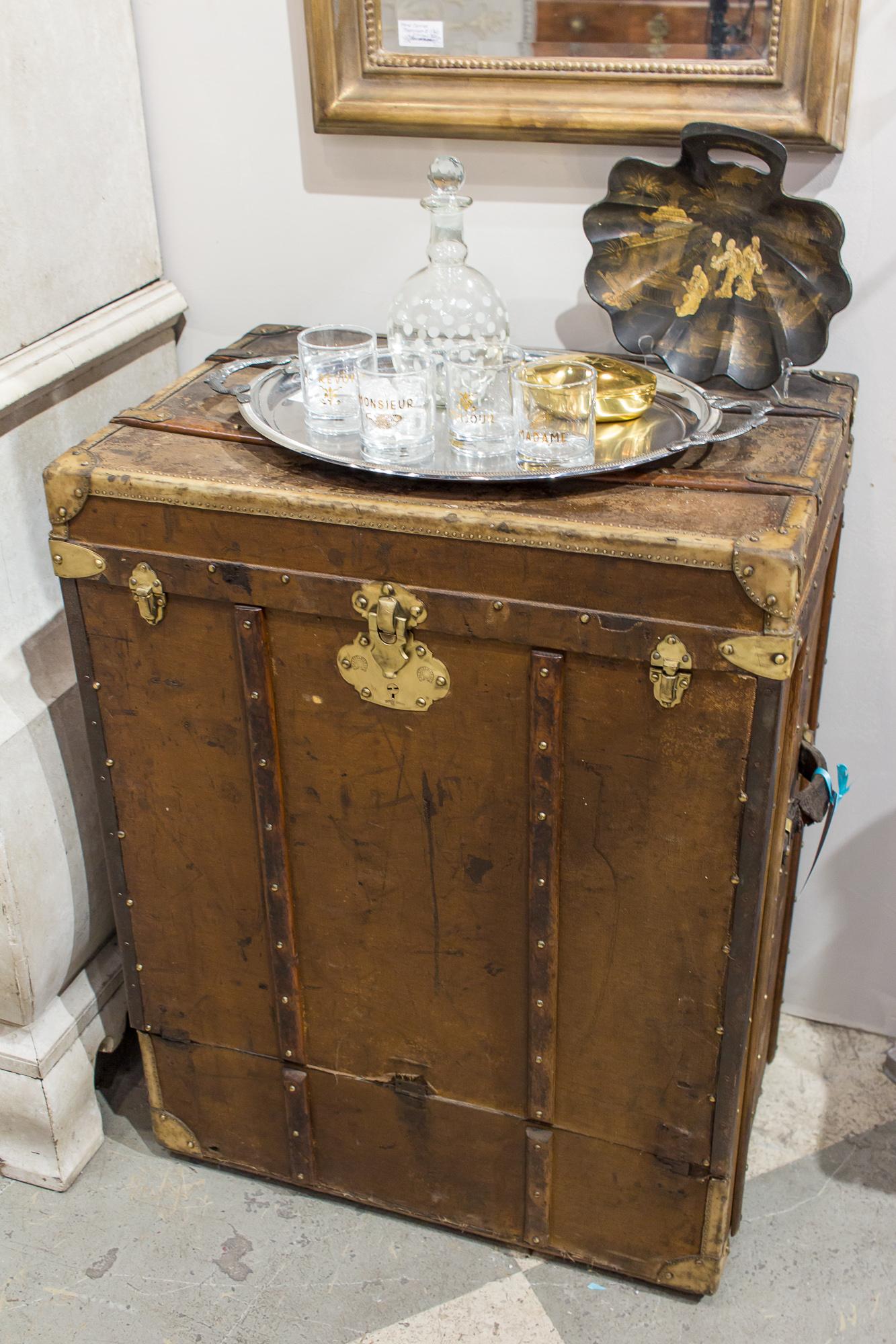 Lorsque nous avons trouvé cette grande malle de style steamer:: nous l'avons imaginée comme un plateau de bar. La malle est fabriquée en bois:: en toile et en cuir:: avec une quincaillerie en laiton. Il y a quelques restes d'étiquettes de voyage sur