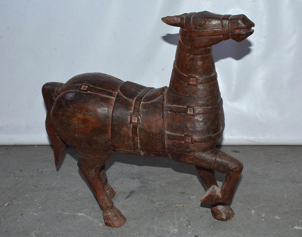 The beautifully hand carved Chinese wood horse is in the style of those produced during the Tang Dynasty. The material is a dark wood with remnant of red paint. Parts were carved separately and then attached, such as the raised front leg and the