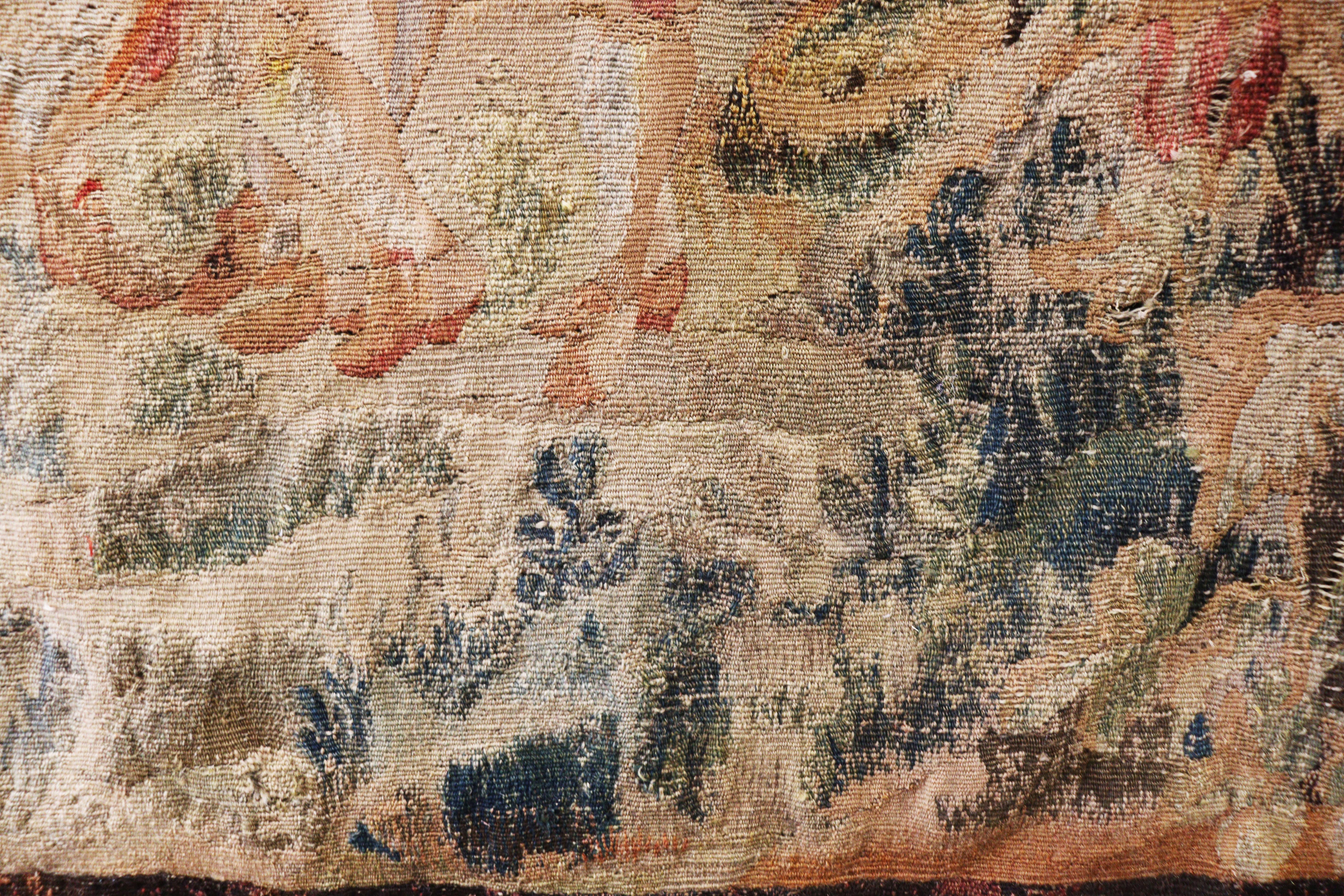 A fine and rectangular tapestry woven in tan and rust tones with green. In the center is a forest landscape.
Made of wool and silk.