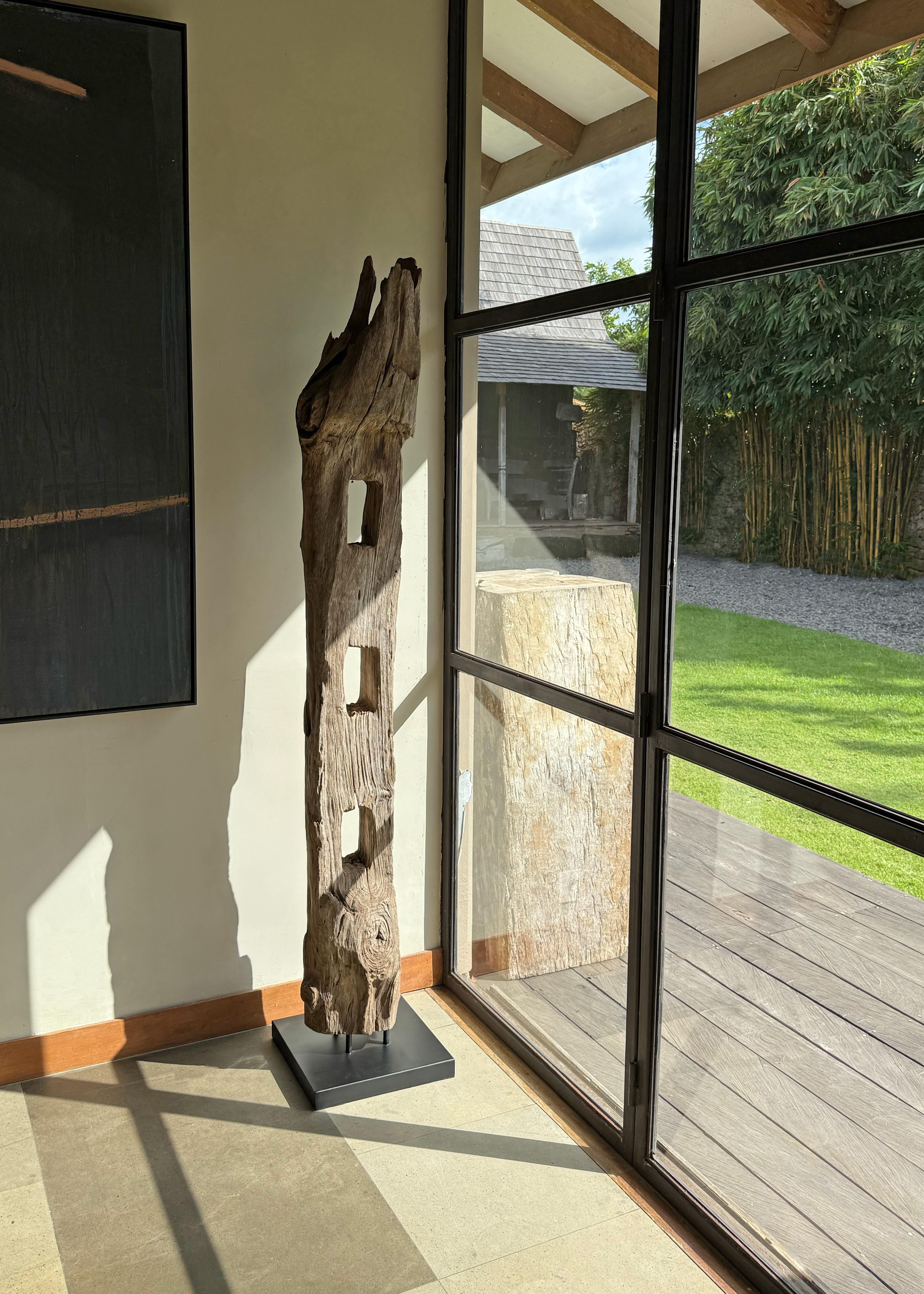 This striking artifact is an antique teak fence column from Java, Indonesia, once part of a traditional cow pen enclosure. Hand-hewn from dense, old-growth teak wood, the column now stands as a sculptural relic of rural craftsmanship and utilitarian