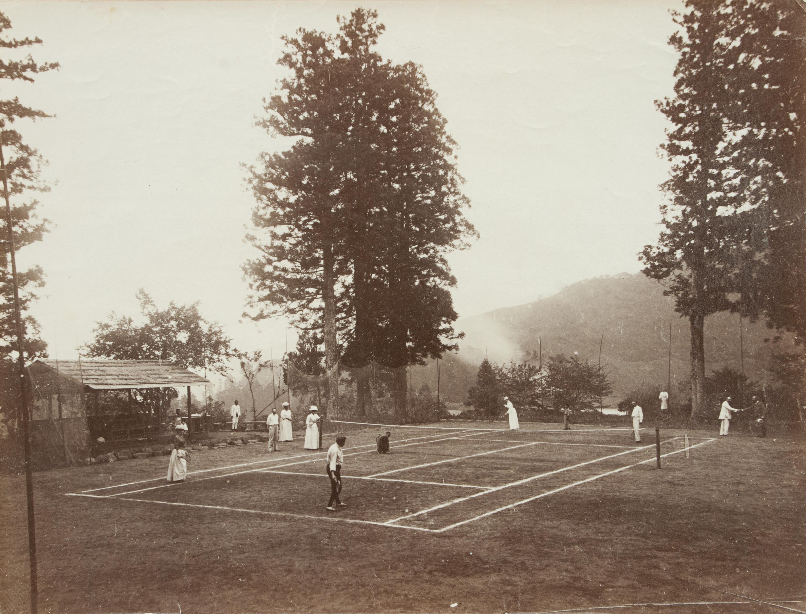 British Colonial Tennis Photograph. This black and white photograph captures the essence of British Colonial life in the late 19th century. The loose albumen print shows a game of mixed doubles in progress. There is a catch net all the way around