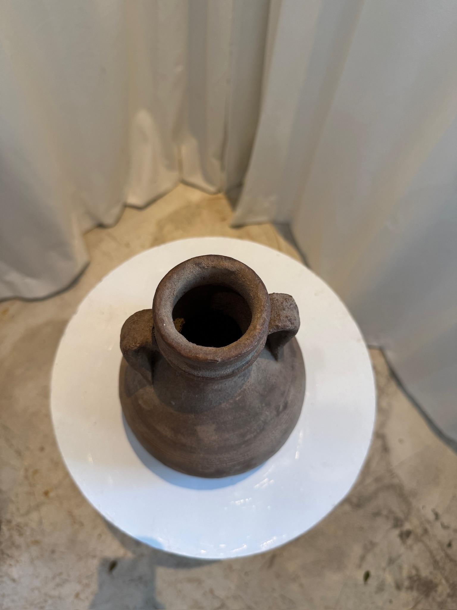 Inspirada en la elegancia intemporal de la cerámica romana clásica, esta antigua vasija de terracota estilo ánfora es una pieza decorativa extraordinaria. Con su cuerpo redondeado, cuello estrecho y asas dobles graciosamente curvadas, se asemeja a
