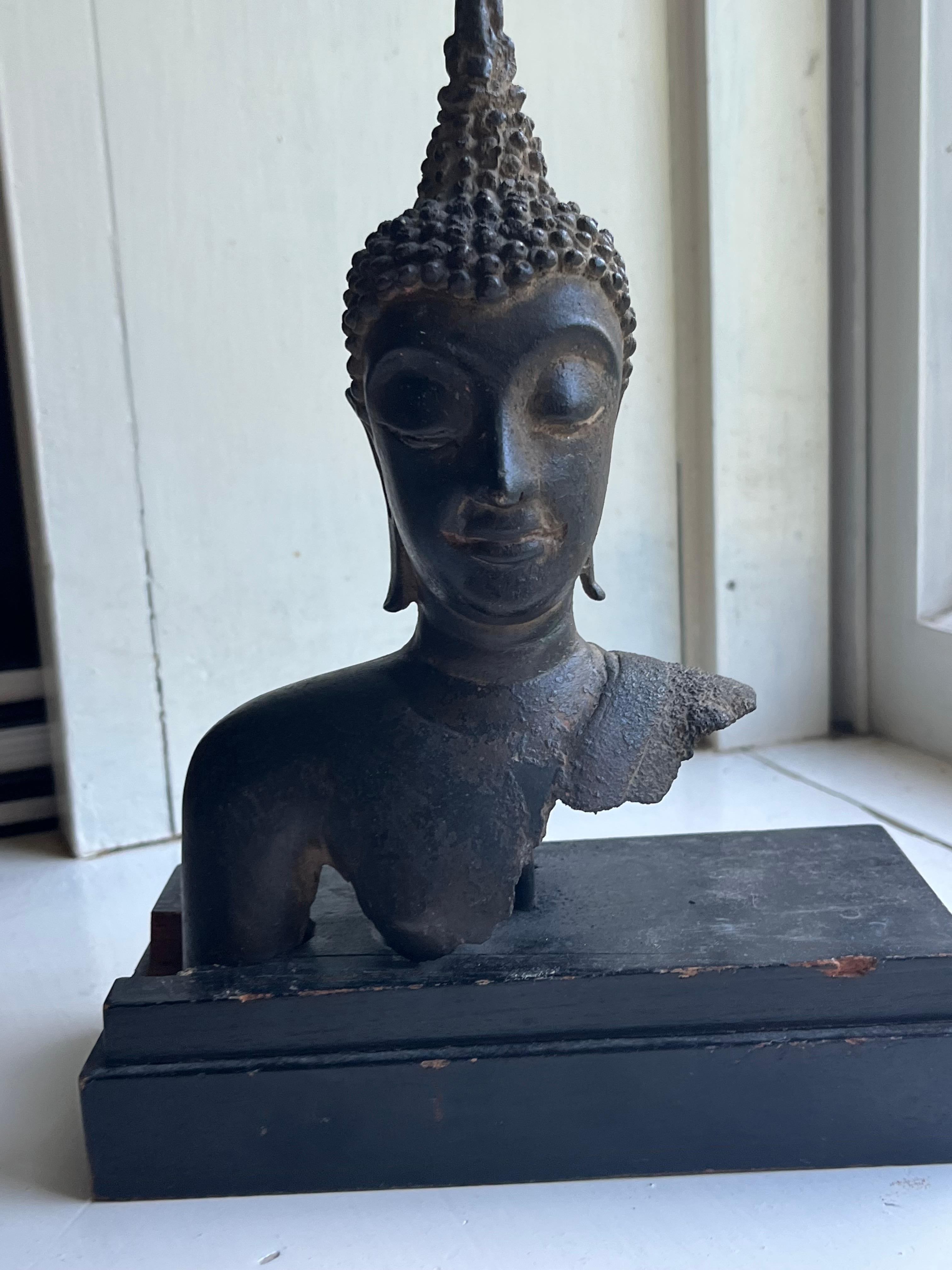 An antique Thai bronze Buddha fragment on an ebonized wood base, nicely cast and patinated 