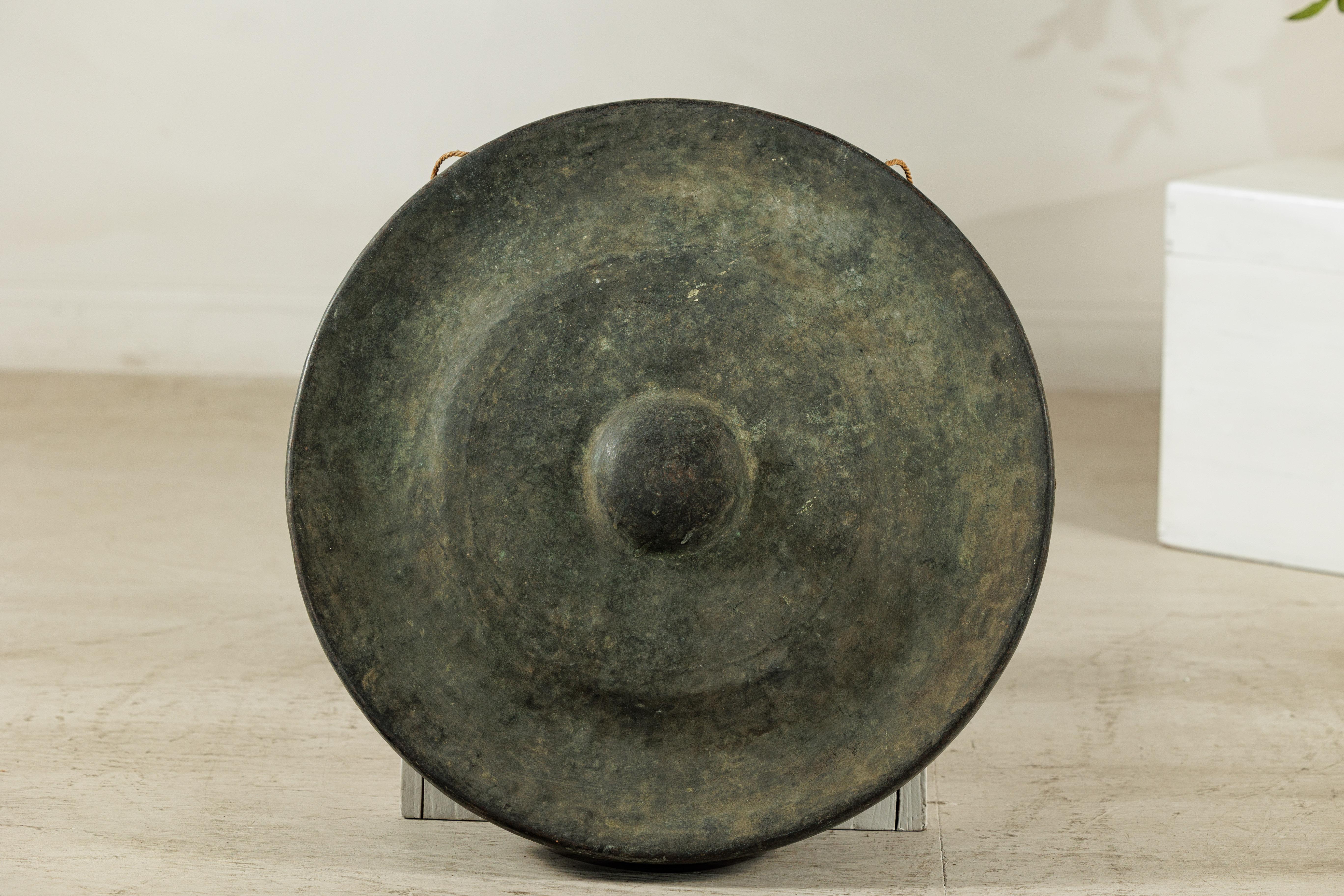 Questo antico gong thailandese in bronzo presenta un accattivante equilibrio tra forma, suono e superficie. Realizzato in bronzo fuso, il pezzo presenta un centro a cupola (o capo) circondato da anelli concentrici in leggera ascesa che ne segnano il