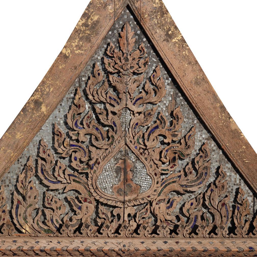Antique Thai Buddhist Temple Pediment. 
An architectural remnant of an assembled teak triangular gable carved with elaborate and symmetrical “kanok” vegetal designs surrounding a central Buddhist gem design having the outline of an image that once