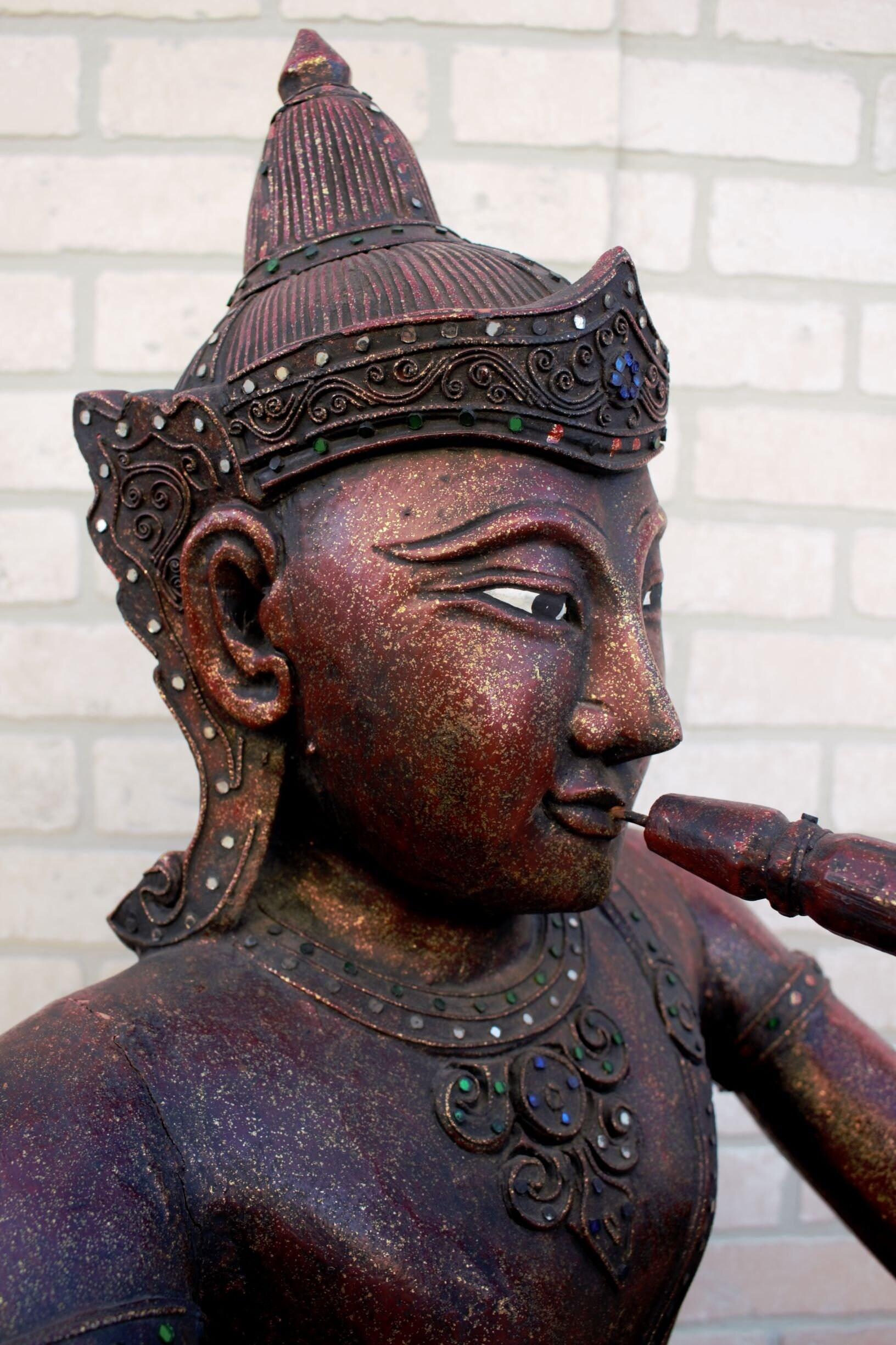Ancien Bouddha assis sculpté thaïlandais jouant de la flûte

Il s'agit d'un Bouddha thaïlandais ancien, avec une base triangulaire correspondant à sa position assise en lotus. Il tient une flûte et est orné de nombreux miroirs et filigranes. Cette