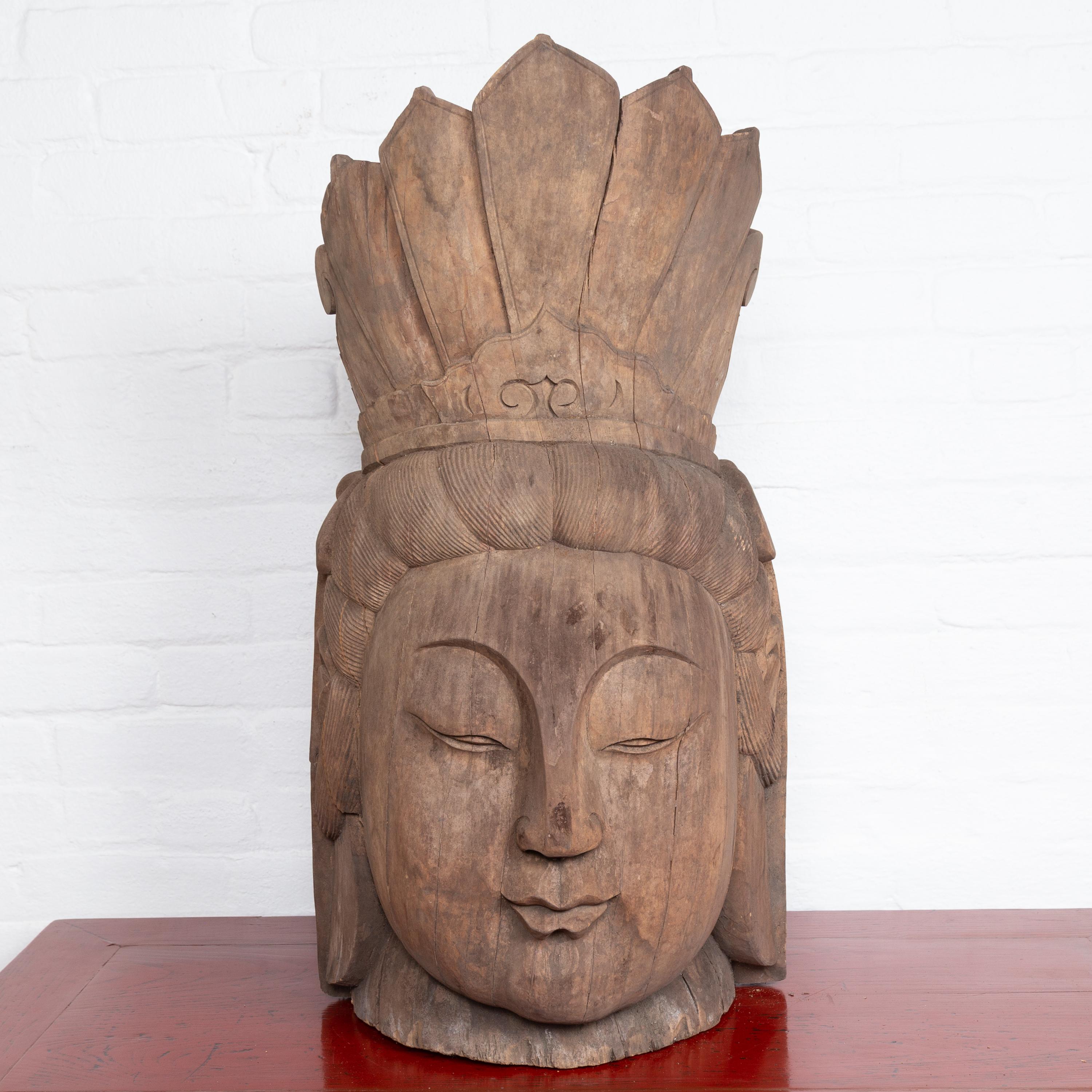 A large vintage Thai carved Chinese design wooden head sculpture depicting Guanyin, the bodhisattva of compassion. Found in Thailand and topped with a tall crown, this Chinese style wooden depiction of Guanyin captivates us with its calm presence.