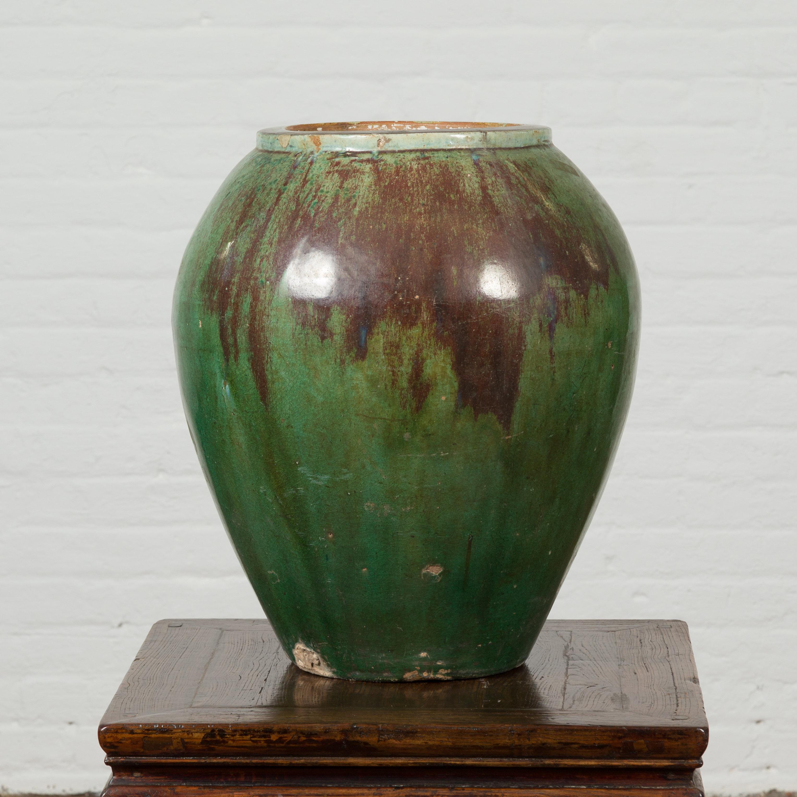 An antique Thai garden vase from the 19th century, with distressed verde patina and drip glaze. Created in Thailand during the 19th century, this garden vase features a distressed verde ground accented with a brown drip glaze. With an opening of