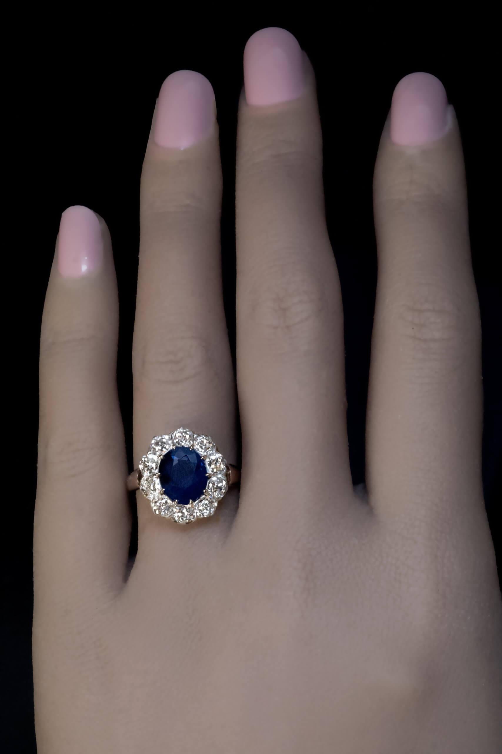 Circa 1910  This classic cluster ring is crafted in gold and platinum. The ring features a 2.11 carat natural unheated Thai sapphire of a medium blue color. The sapphire is surrounded by chunky old mine cut diamonds (VS1-VS2 clarity, average – K