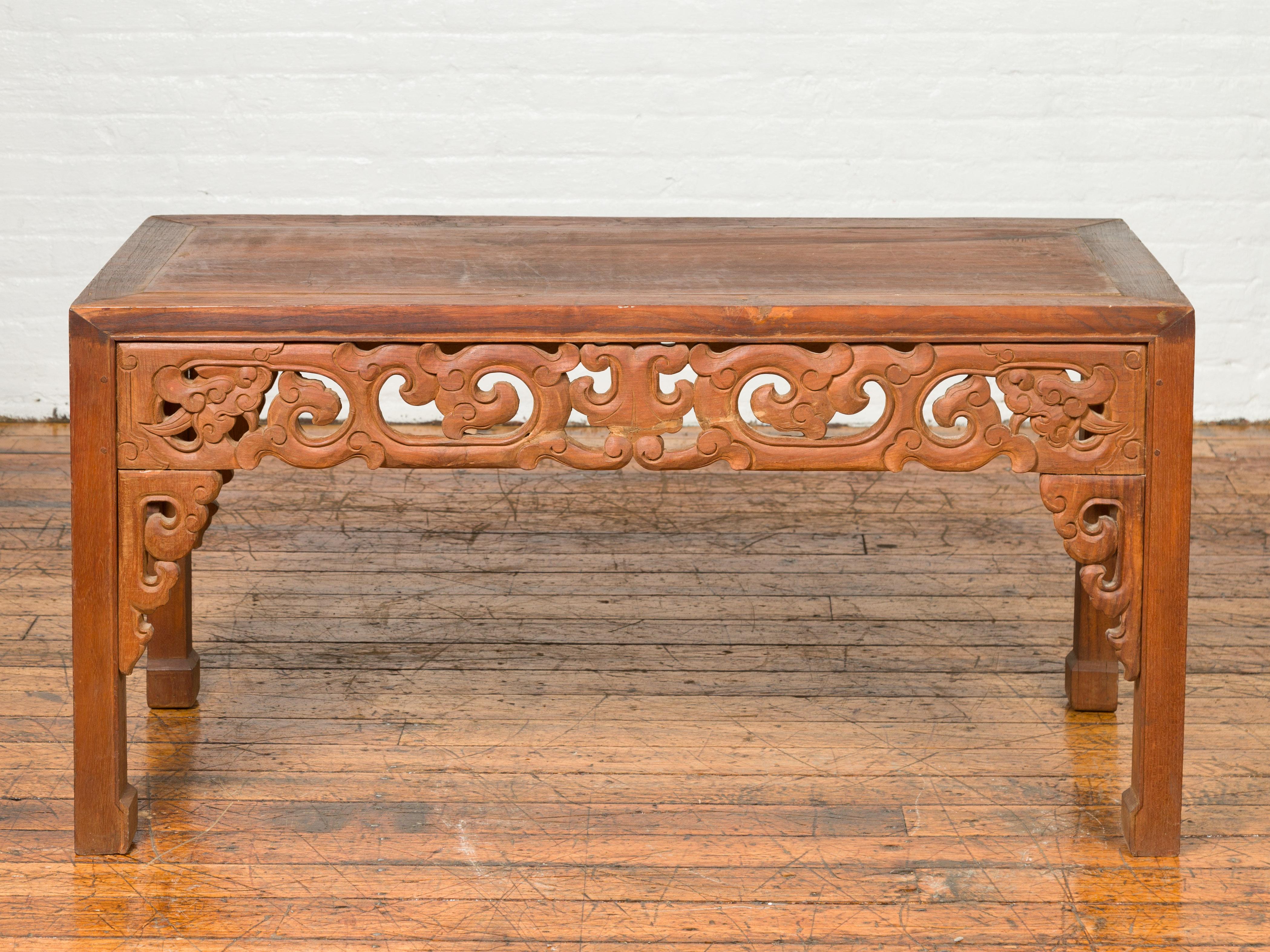 An antique Thai teak side table from the early 20th century, with carved apron and horse hoof extremities. Charming our eyes with its clean lines and handsome apron carved with scrolling cloud motifs, this side table features a rectangular top and