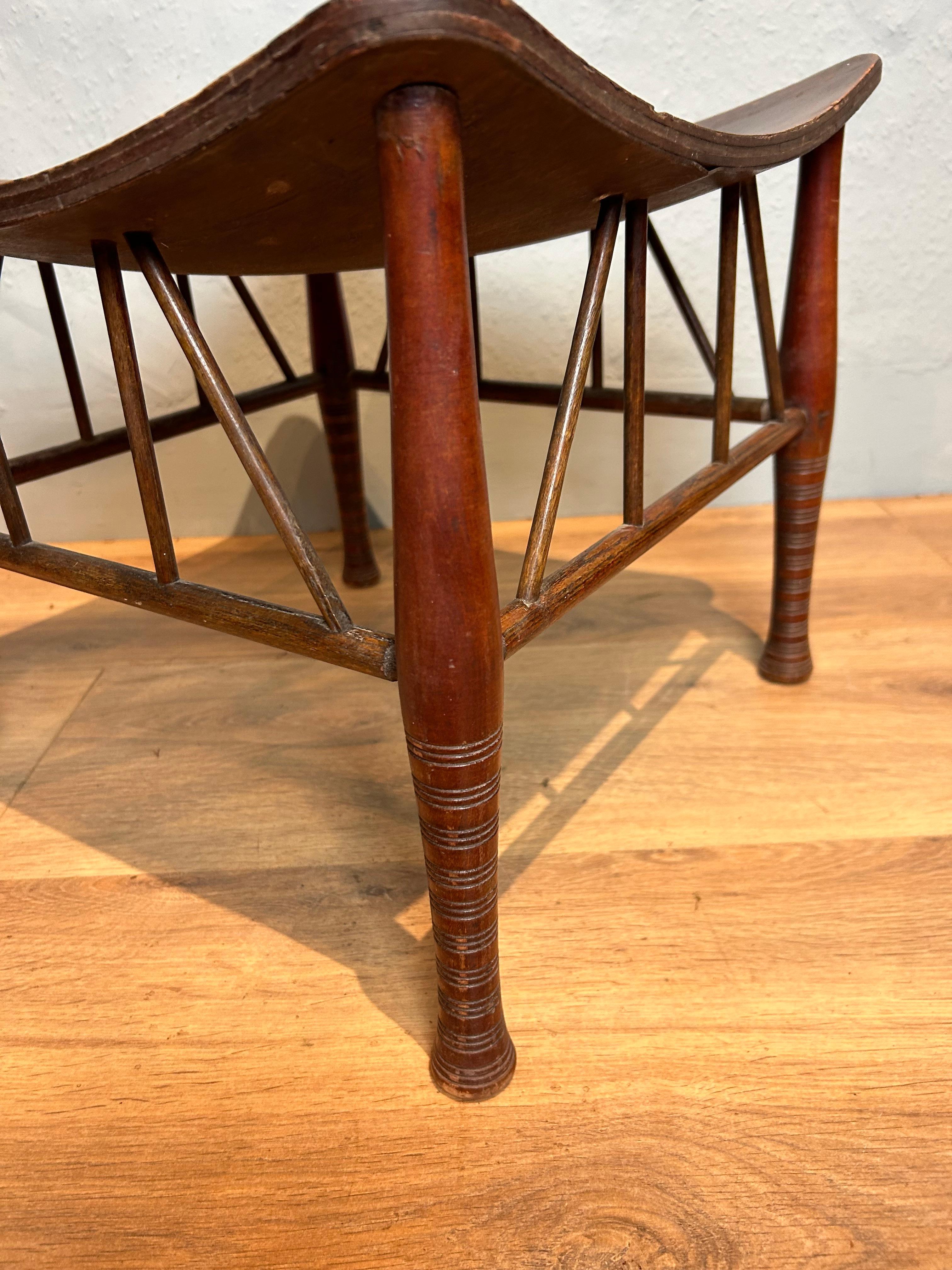Antique Thebes stool circa 1910, probably retailed by Liberty of London. The design is based on an Egyptian stool which dates back to 1400BC. This attractive stool has a plywood dished top resting on turned legs with supporting lattice bracing,