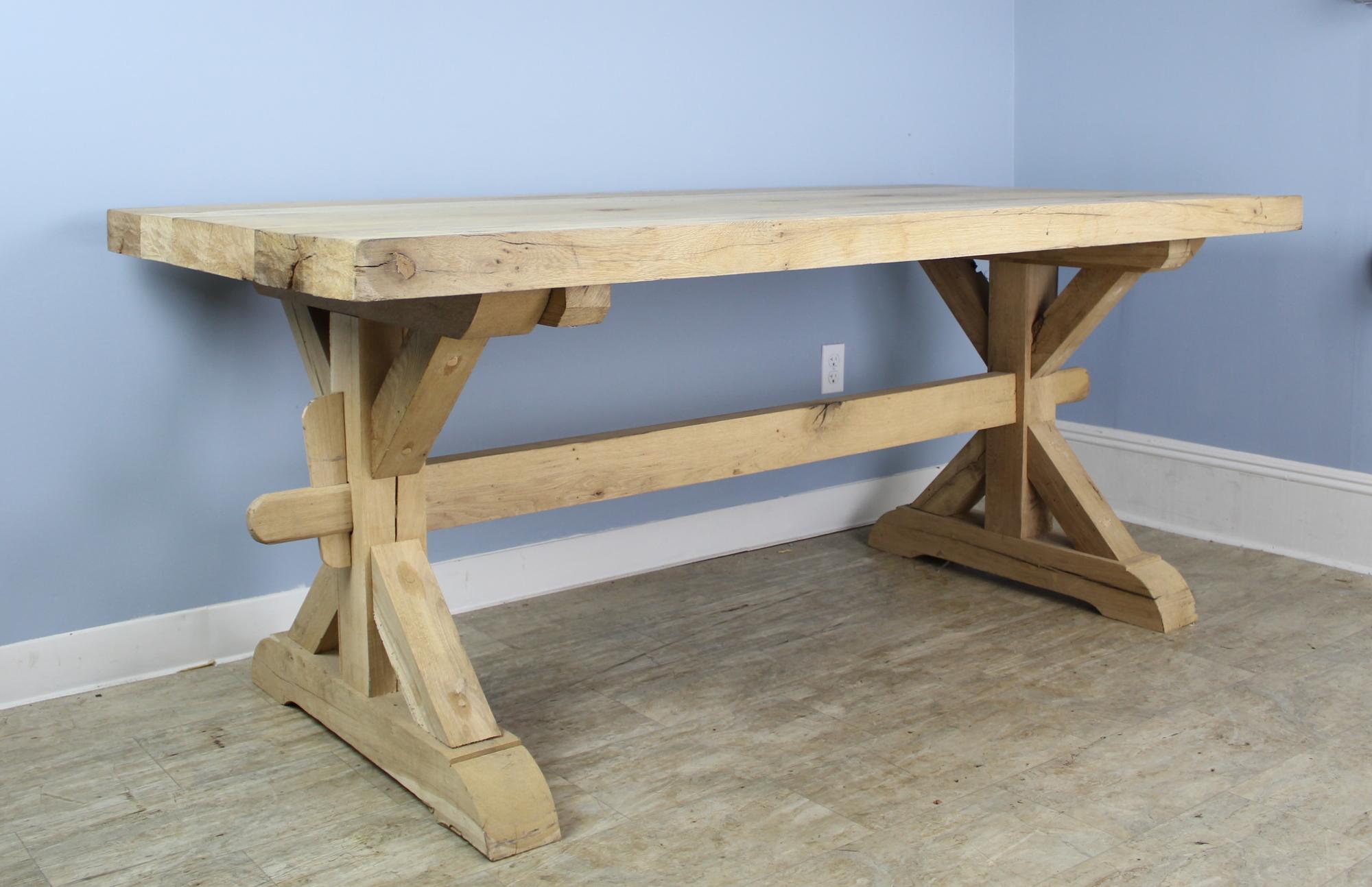 A handsome bleached oak farm table with an Arts & Crafts style trestle base and a 2.5 inch thick top. The piece has very good oak grain throughout and the light wood gives it a modern sensibility. No apron or legs means this table can accommodate 8
