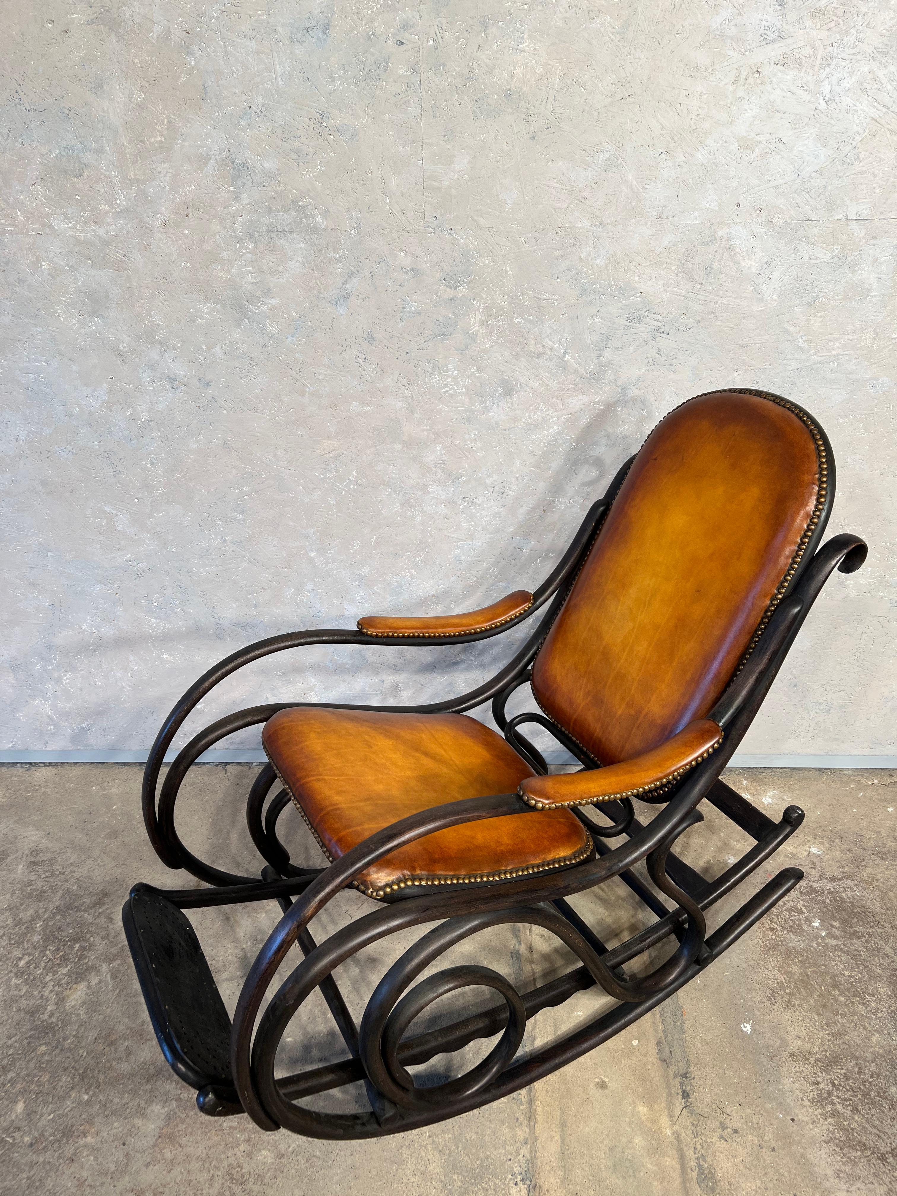 Rocking chair, original from the early 1900 Art Nouveau, with ebonised curved beech frame, upholstered seat, back and armrests.

Restored and reupholstered in leather of excellent workmanship in a patinated tan colour, the contrast is stunning. In