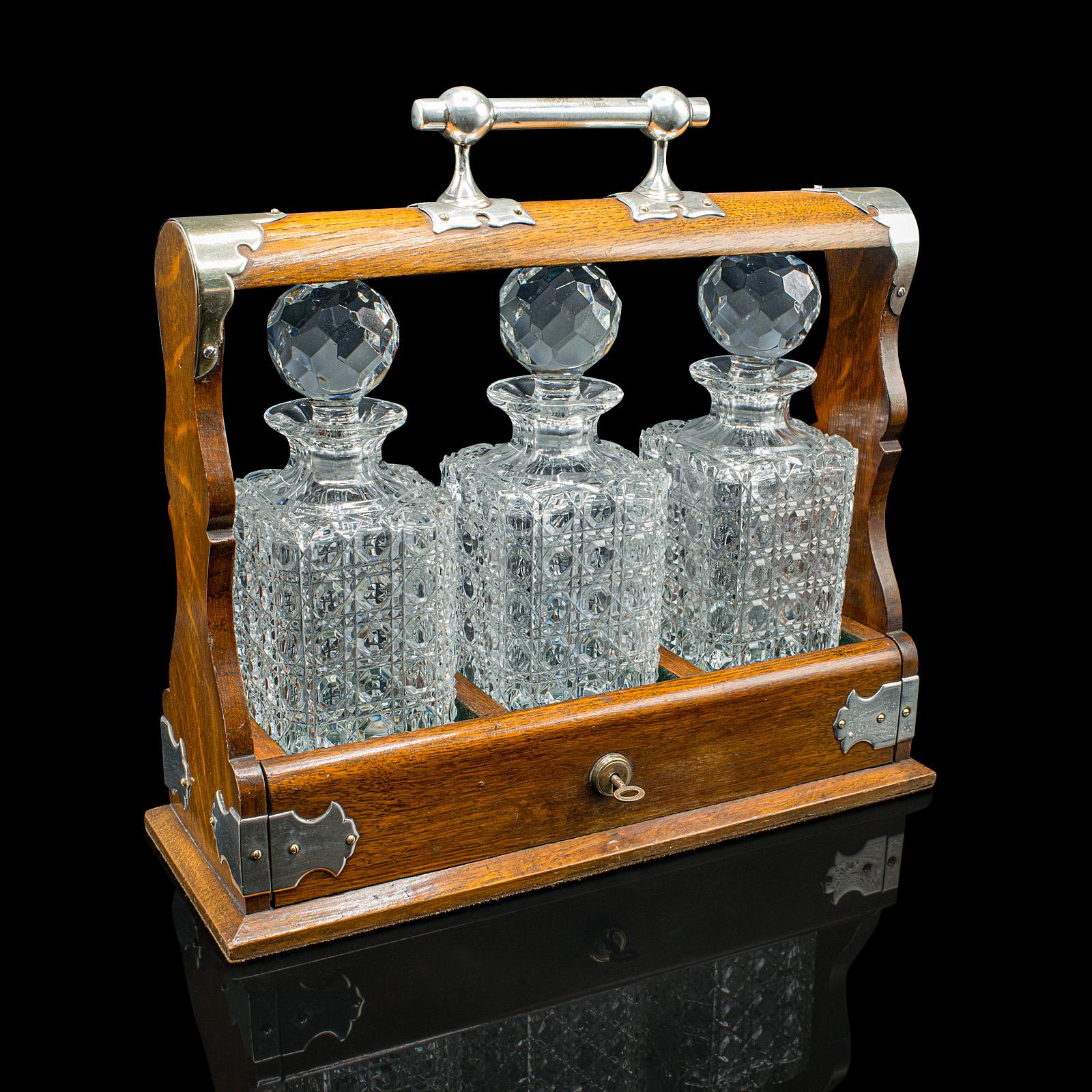 This is a distinguished antique three bottle Tantalus. An English, oak and silver plated drinks caddy with a trio of cut glass decanters, dating to the late Edwardian period, circa 1910. A fine prize-given example, offering refined decorative appeal
