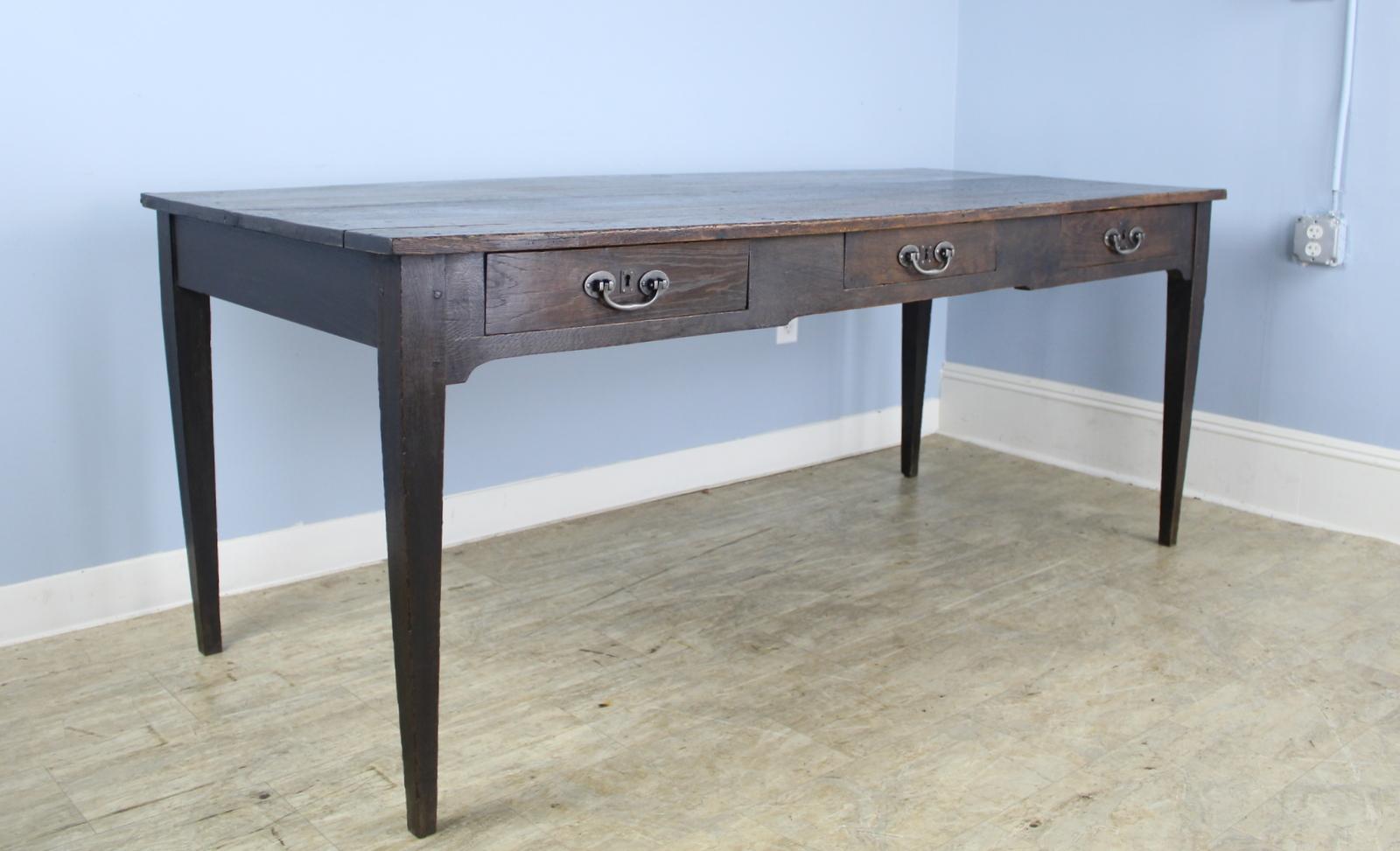 A classic dark oak farm table with three roomy drawers in the apron. There is a small area of old wear at the edge of the table top, shown in the thumbnails. Iron drop handles are new. Apron height of 24 inches is good for knees and there are 70.5