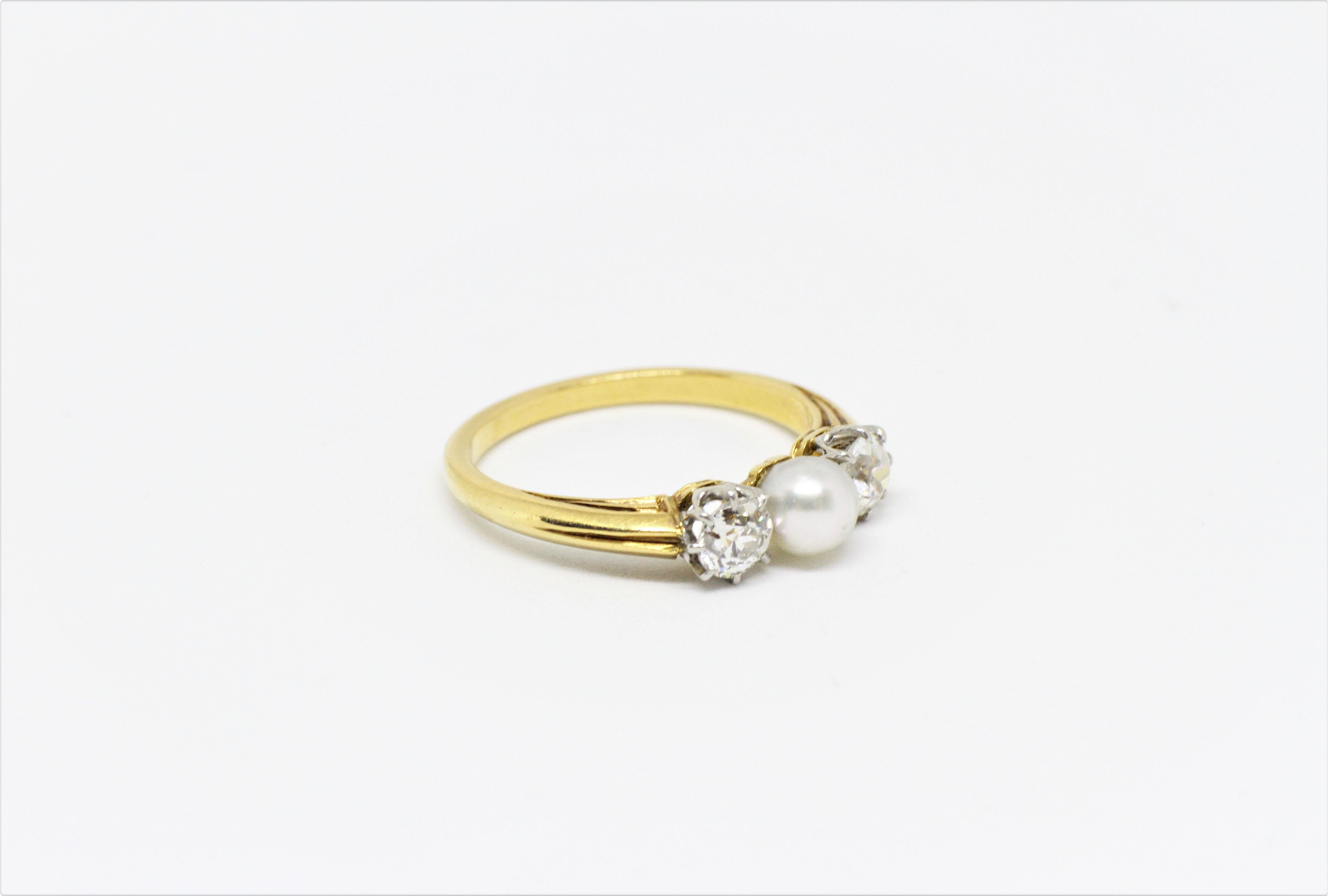 Classic early 1900's three stone ring set with a white natural pearl in the centre of approximately 4.6 millimeters, accompanied by two old cut diamonds of approximately 0.25 carats each on either side. The diamonds are mounted in 7 platinum claws