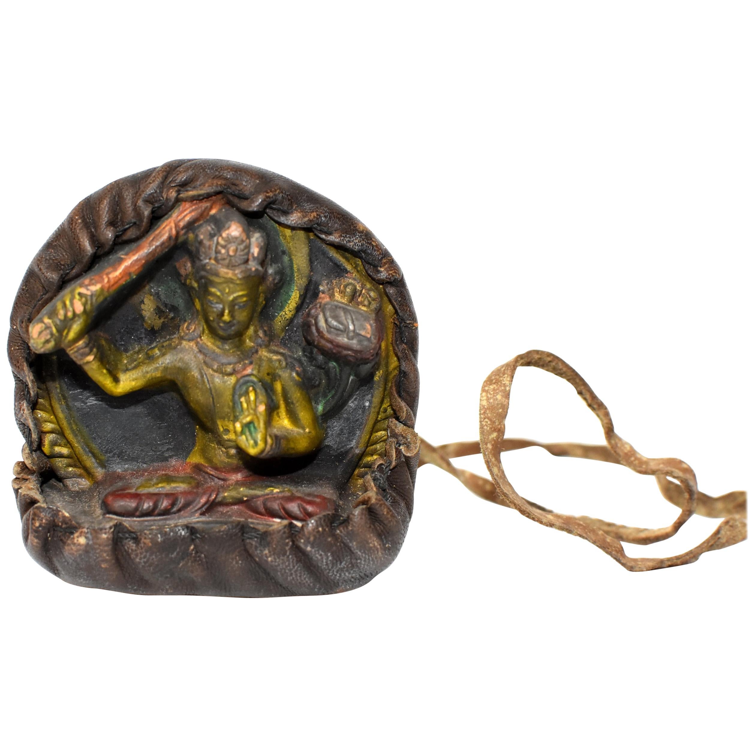 A Tibetan amulet featuring Tara encased in a handmade leather shrine. The Tara is made of terracotta, beautifully crafted displaying well defined facial features, decorated robe and a wonderful smile. Featured is the Tara holding sword, symbolizing