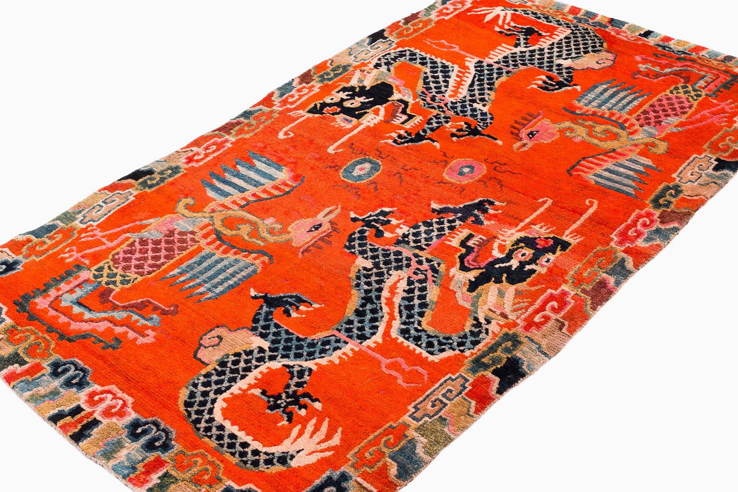Ce petit tapis ancien Khaden est remarquable pour son champ orange fantastique et son design expressif. Deux phénix et deux dragons s'équilibrent de part et d'autre. Dans les mythologies tibétaine et chinoise, le dragon et le phénix sont souvent