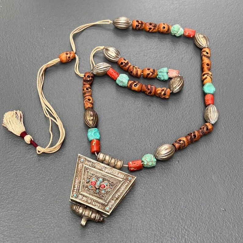Una rara e affascinante collana Gau Amulet Box tibetana, con un ciondolo a forma di scatola amuleto dal design intricato con una montatura in lega d'argento, arricchita da turchesi, perle di corallo autentico e perle di teschio intagliate. Il