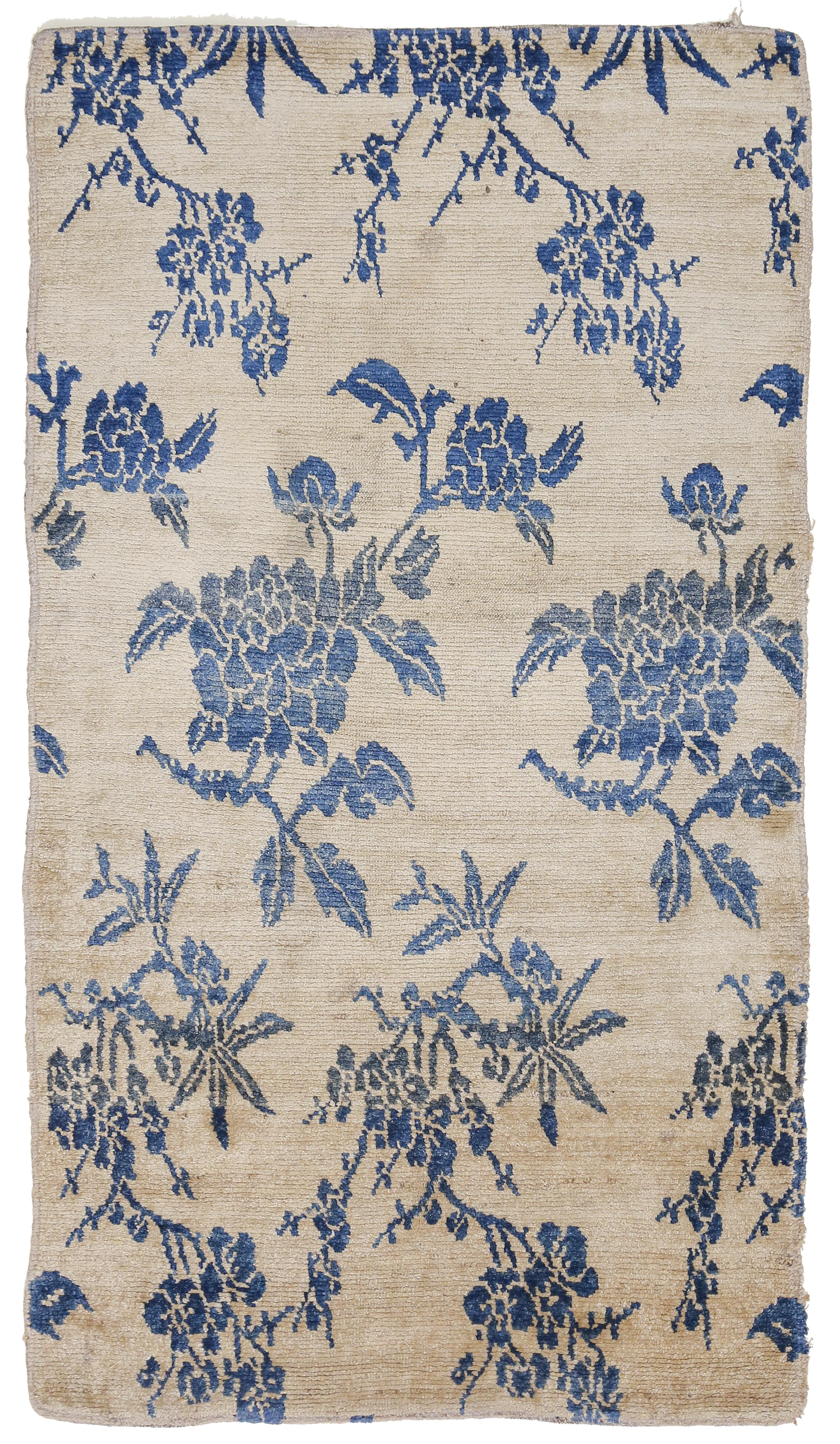 A rare and elegant Tibetan rug in the khaden format distinguished by a beige background decorated by indigo blue scrolling peony flowers. The khaden format indicates that it was originally intended as a meditation rug for High Lamas in the Buddhist