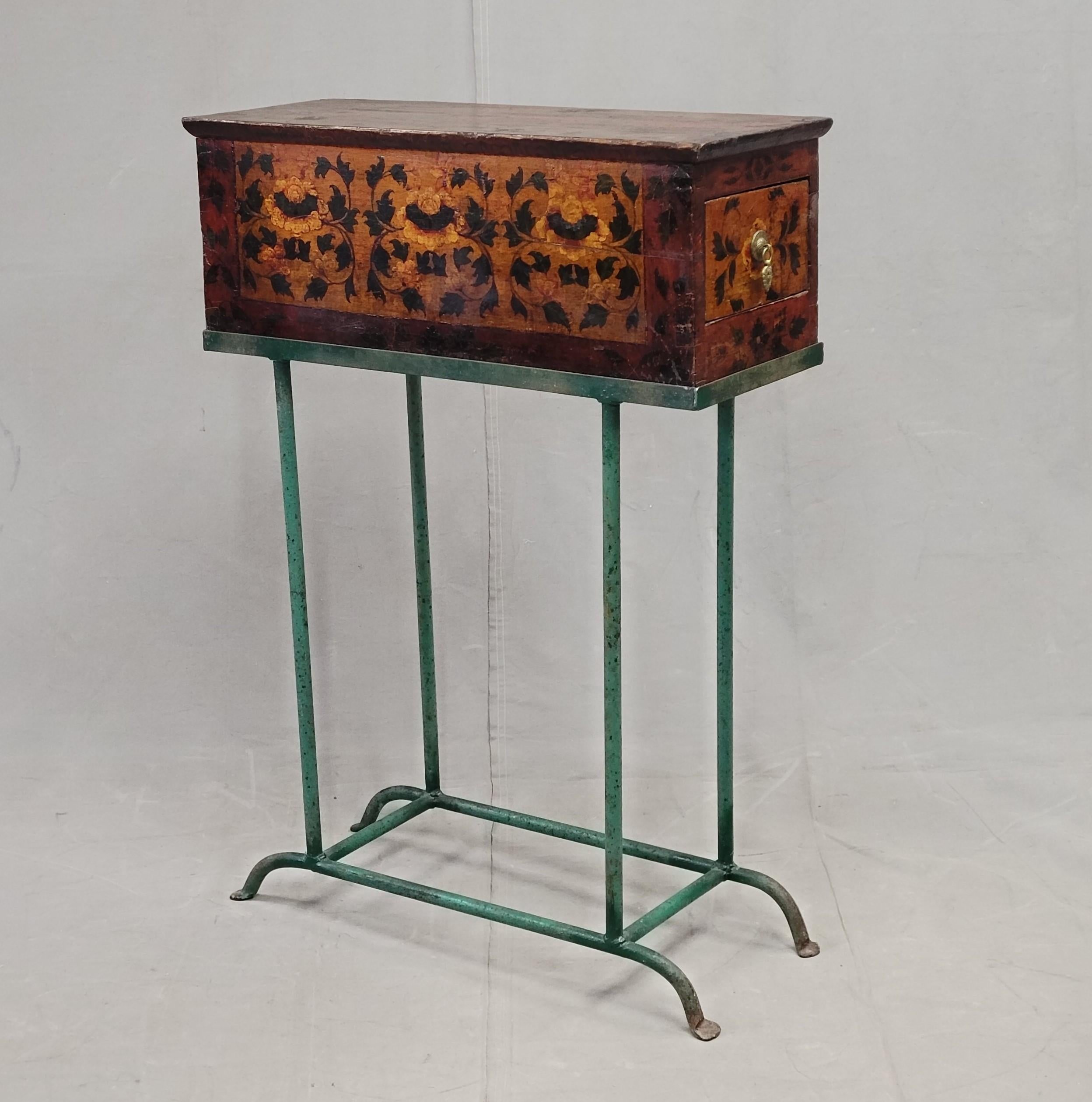 A beautiful antique Tibetan altar box with drawer sits on top of a custom made green metal stand to create a charming small console table. The wood box has a lotus motif and is lacquered in shades of rich brown, deep gold, dark red, and green. Pull