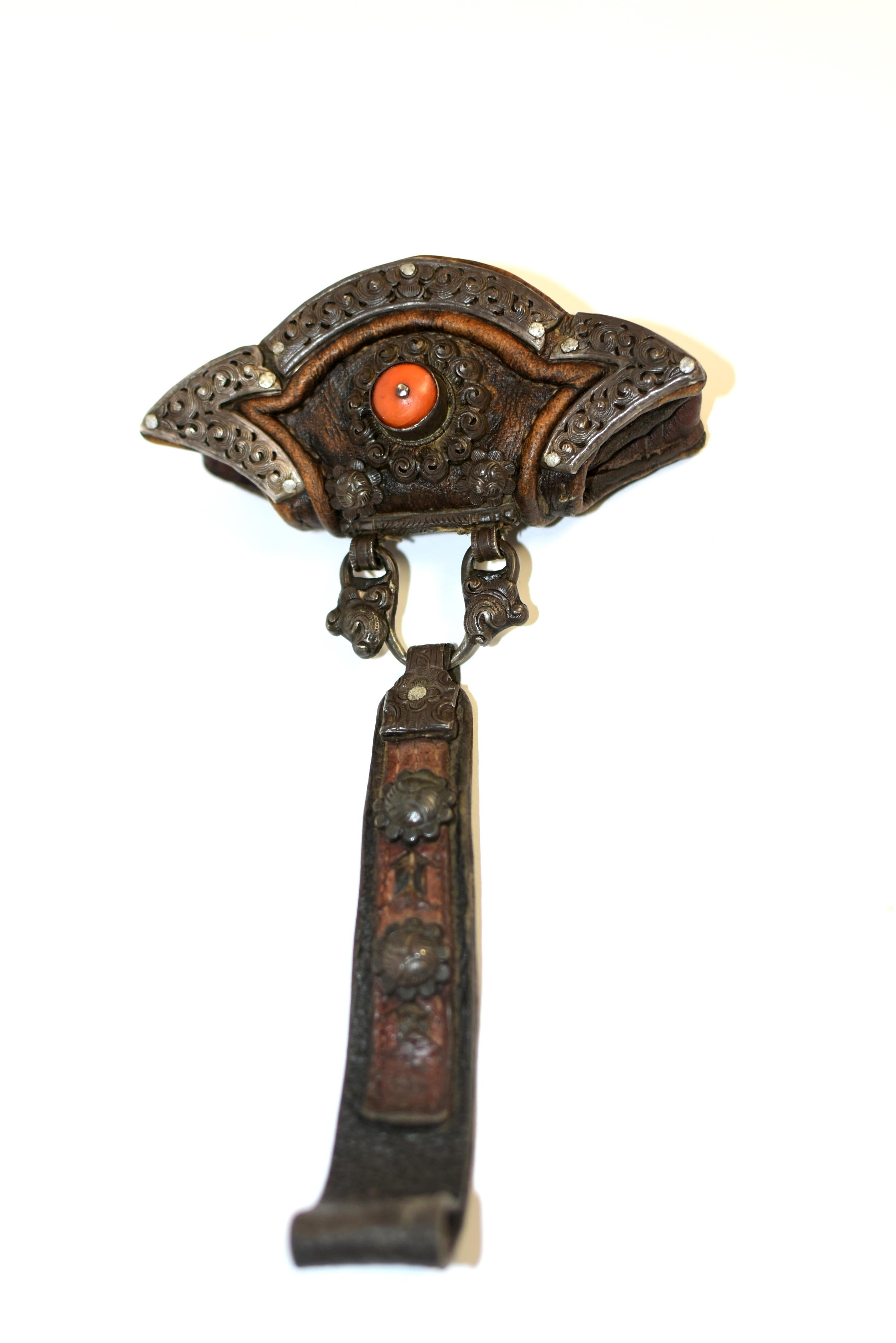 A very rare, completely hand made piece from Tibet. Made of thick leather with embellishments of silver flowers, the front of the pouch features a highly valuable antique Tibetan coral bead surrounded by a ring of silver metal scrolls. Another