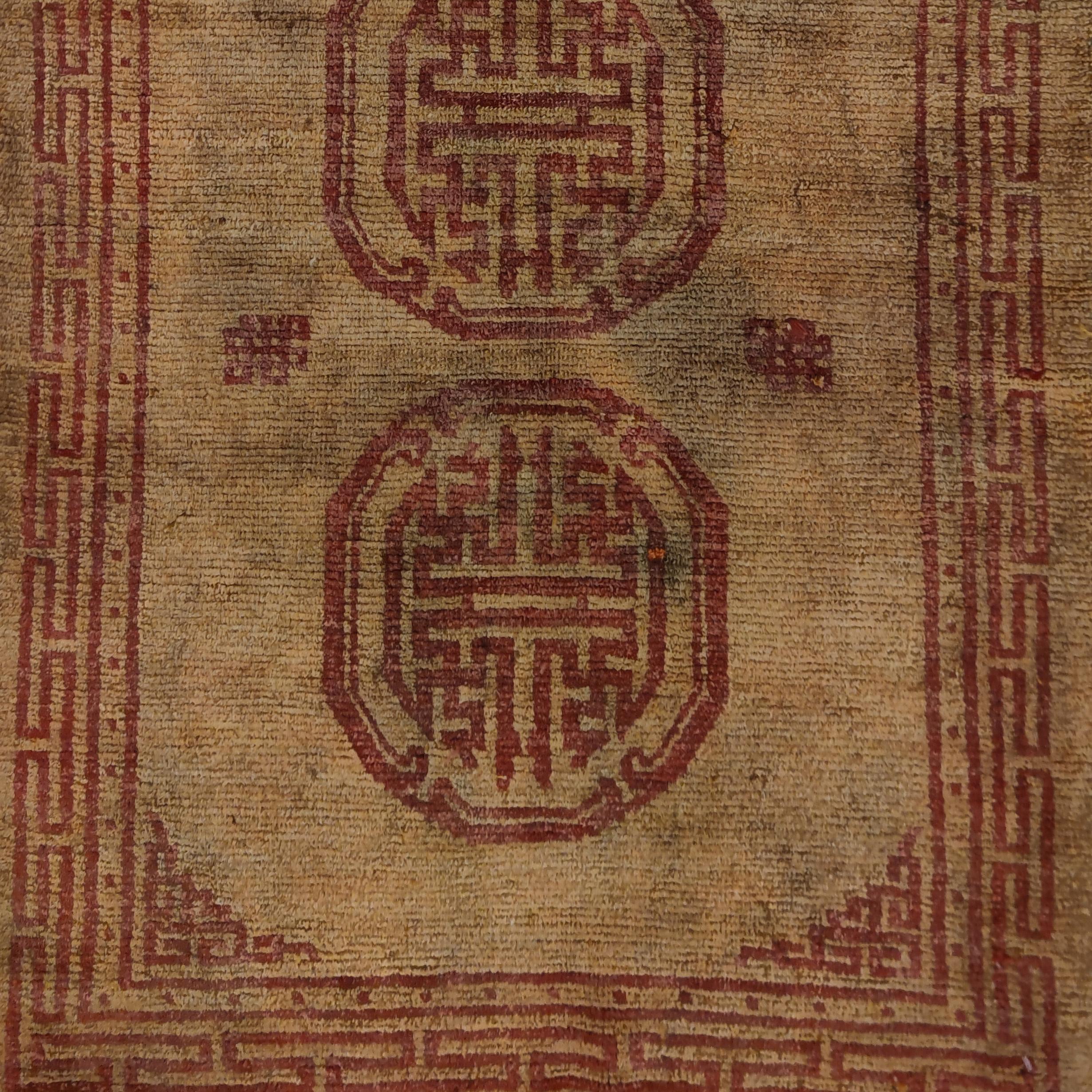 Un tapis tibétain rare et unique, qui se distingue par un fond jaune doux sur lequel se superpose un motif rouge clair composé de trois mandalas, symboles de l'univers. Les tapis dans ces couleurs monastiques étaient utilisés comme tissage de