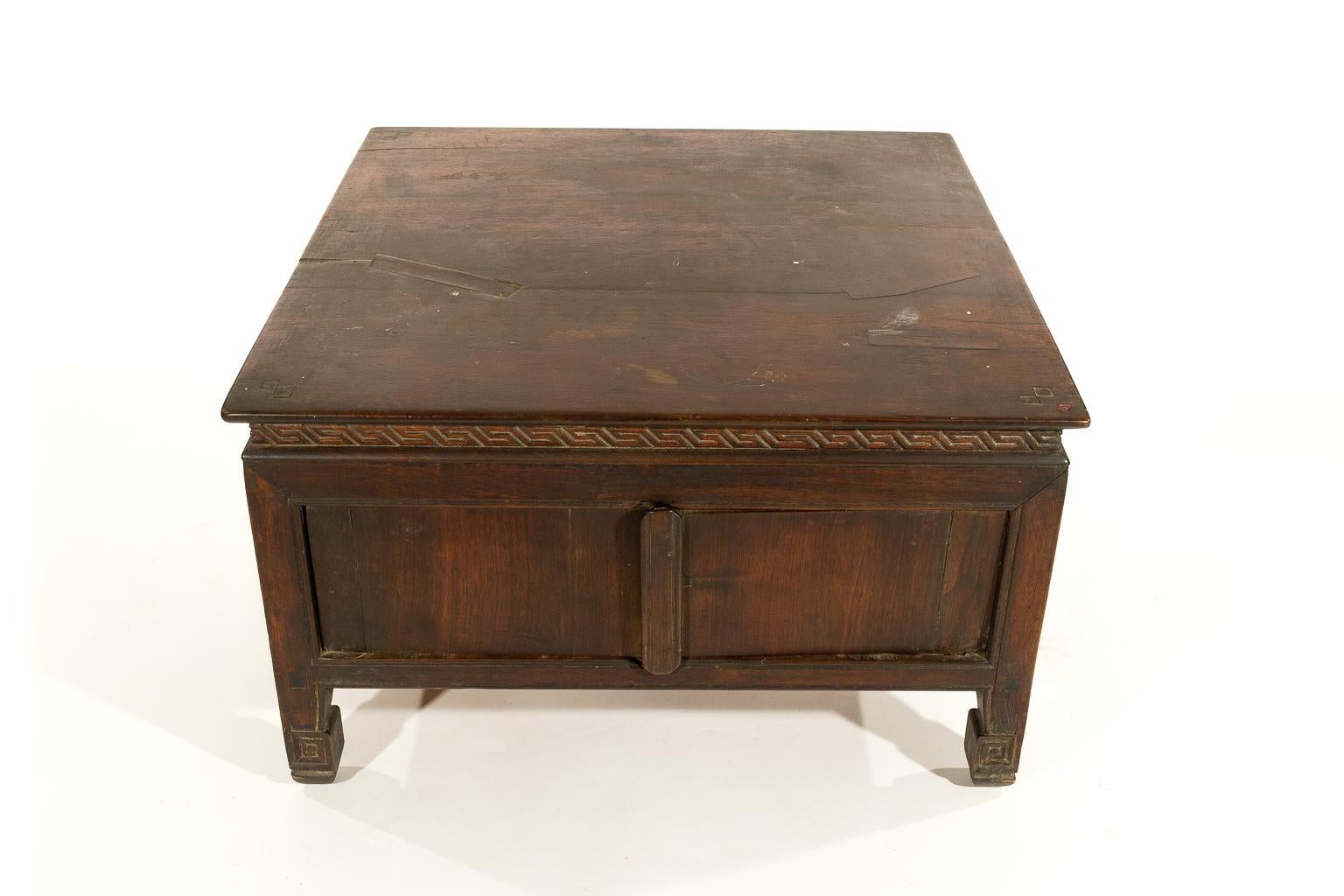 A handmade antique Tibetan tea or coffee table with carved details on the legs and around the tabletop. The table has doors that open into a storage area. It is very rustic as it came from a wealthy Tibetan household in the western part of Tibet.