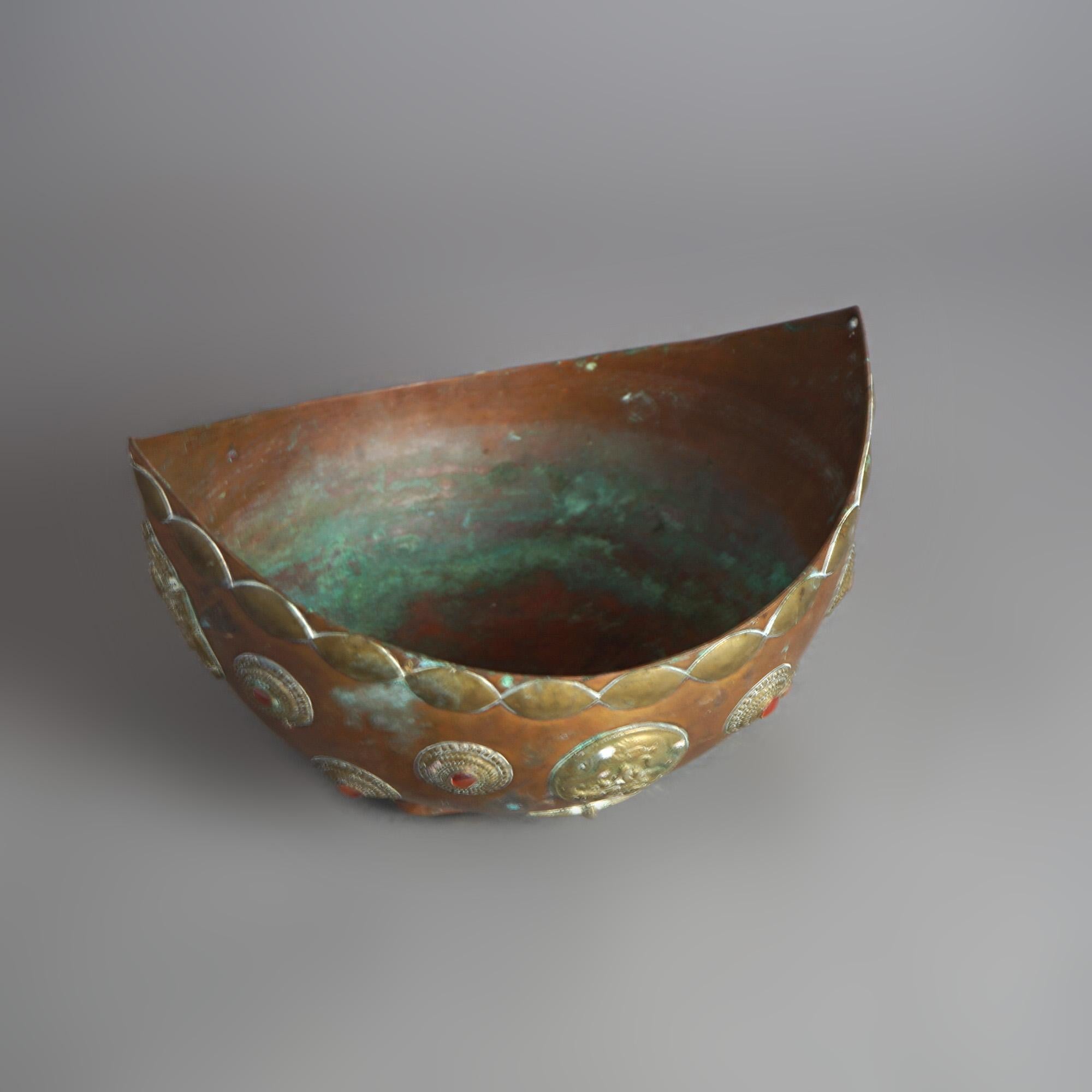 An antique Tibetan ceremonial bowl offers copper construction with medallions, jewels and figural castings, 19th century

Measures- 6.5''H x 10.5''W x 8.5''D