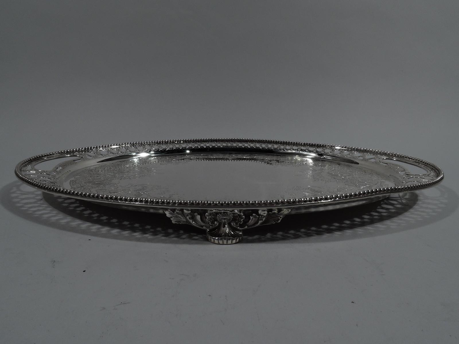 Aesthetic sterling silver salver. Made by Tiffany & Co. in New York. Oval well with vacant center surrounded by engraved ornament: semi-abstract flowers and scrolls spilling over beaded rinceaux border. Curved shoulder with open floral diaper and