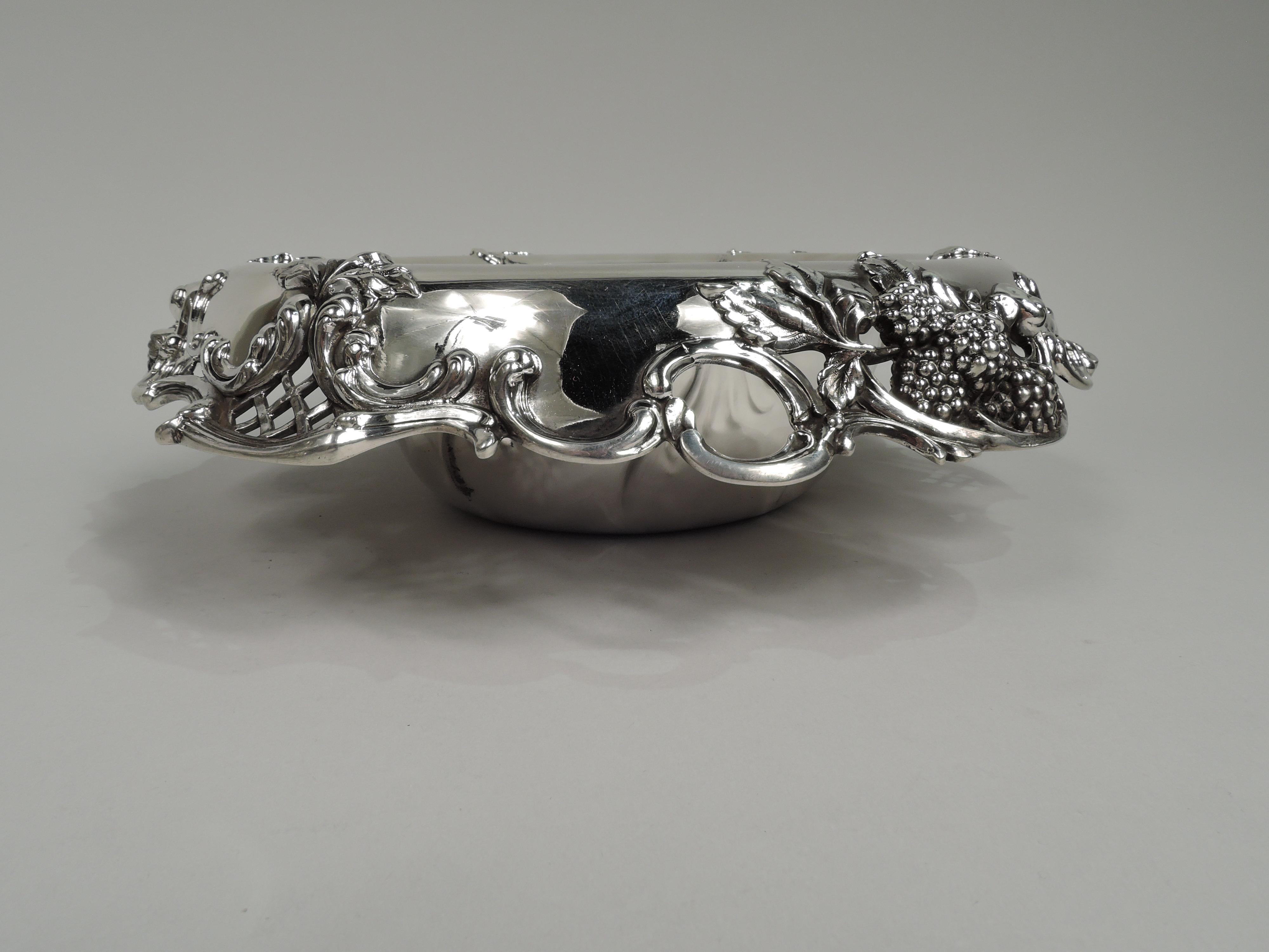 Gilded Age sterling silver berry bowl. Made by Tiffany & Co. in New York. Round with chased outsized leaf border. Scrolled and open turned down rim with applied c-scrolls, leaves, berries, and diaper. A great high-low design with wild fruit wrought