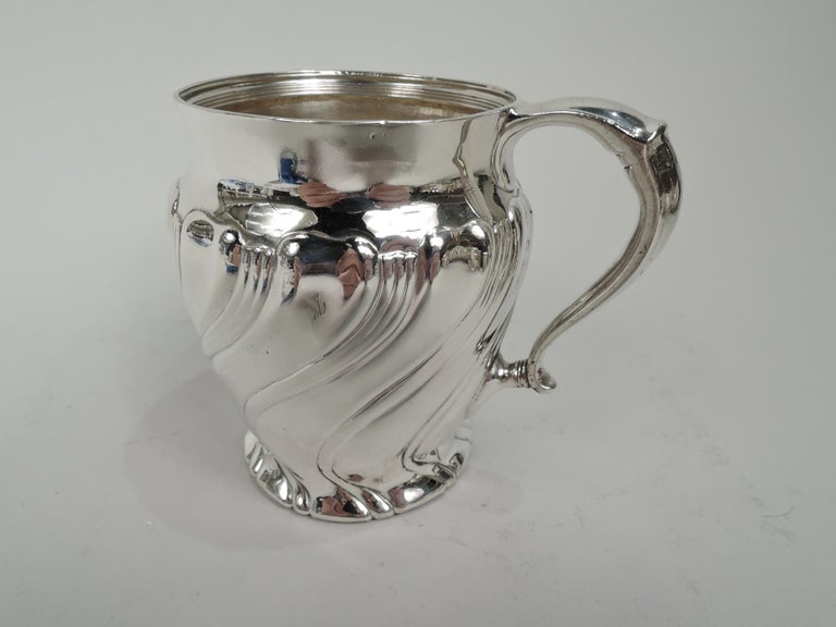 Victorian Classical sterling silver baby cup. Made by Tiffany & Co. in New York, ca 1892. Curved and tapering sides flowing into spread foot; short and plain neck and capped scroll handle. Twisted flutes alternating with twisted reeding. Fully