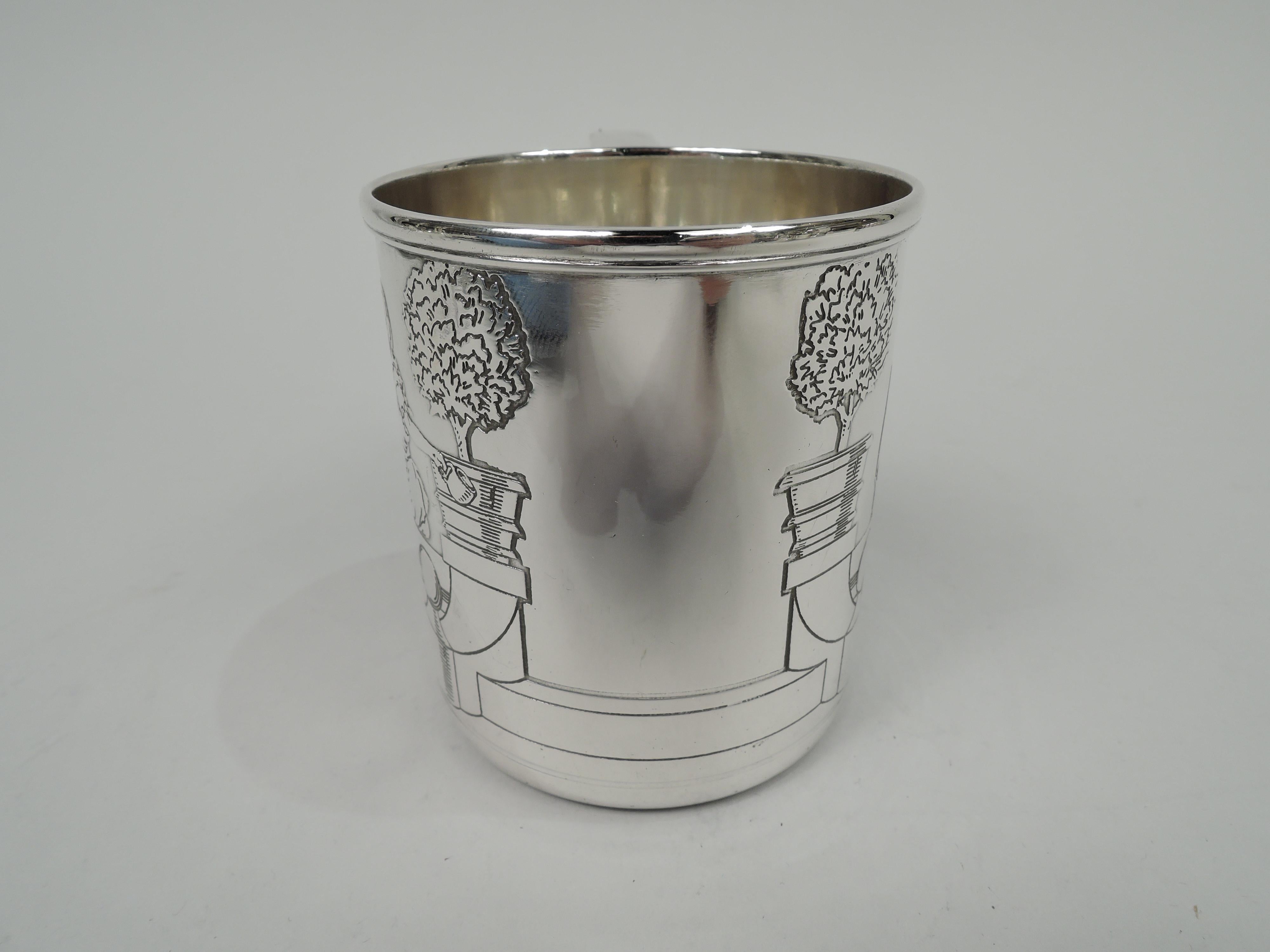 Art Deco sterling silver pictorial baby cup. Made by Tiffany & Co. in New York, ca 1920. Straight sides, molded rim, and scroll bracket handle. Acid-etched scene: A boy and girl perch on top a terrace wall. The boy baits the dog with a treat. The