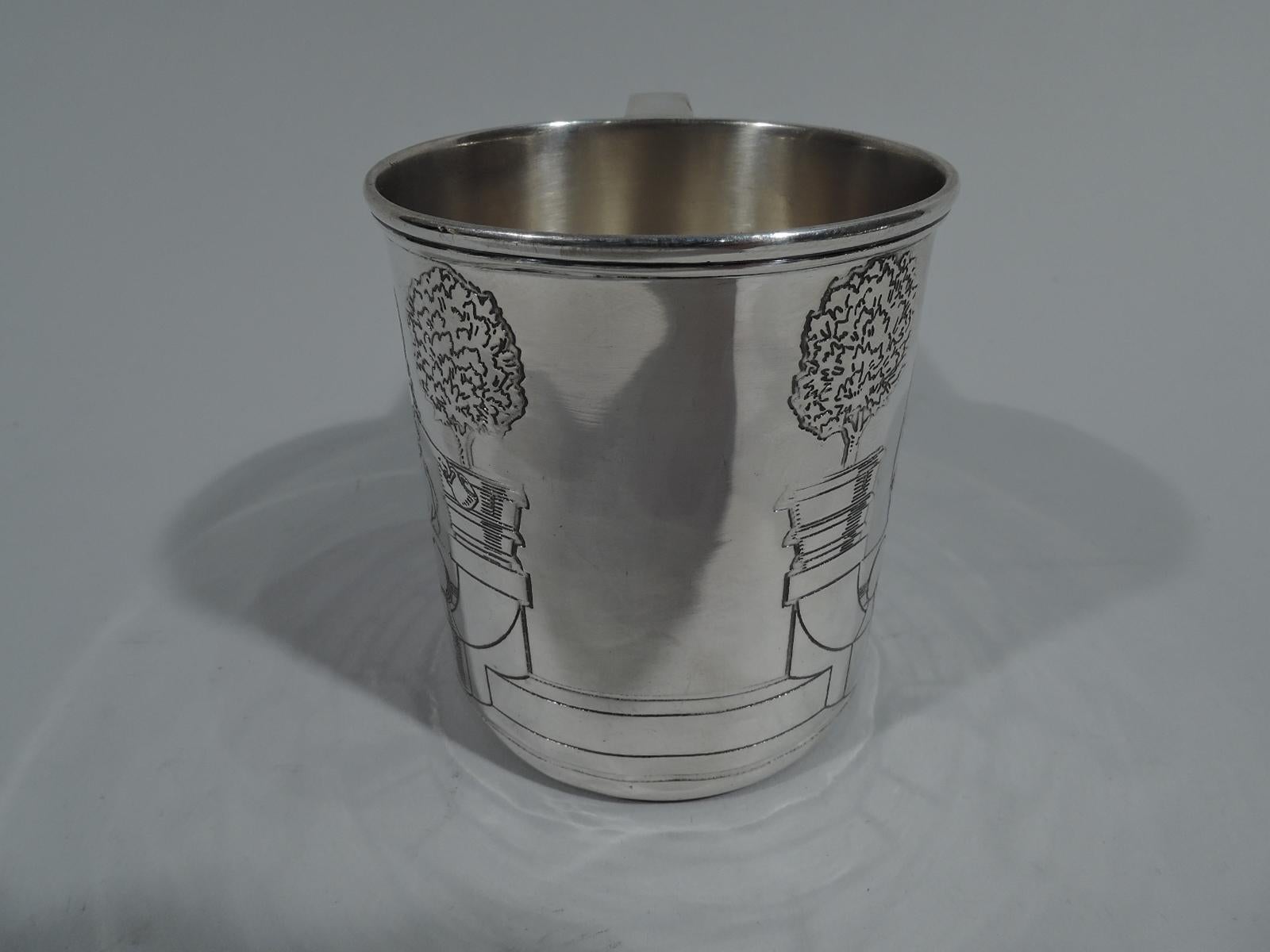 Art Deco sterling silver pictorial baby cup. Made by Tiffany & Co. in New York, circa 1920. Straight sides, molded rim, and scroll bracket handle. Acid-etched scene: A boy and girl perch on top a terrace wall. The boy baits the dog with a treat. The