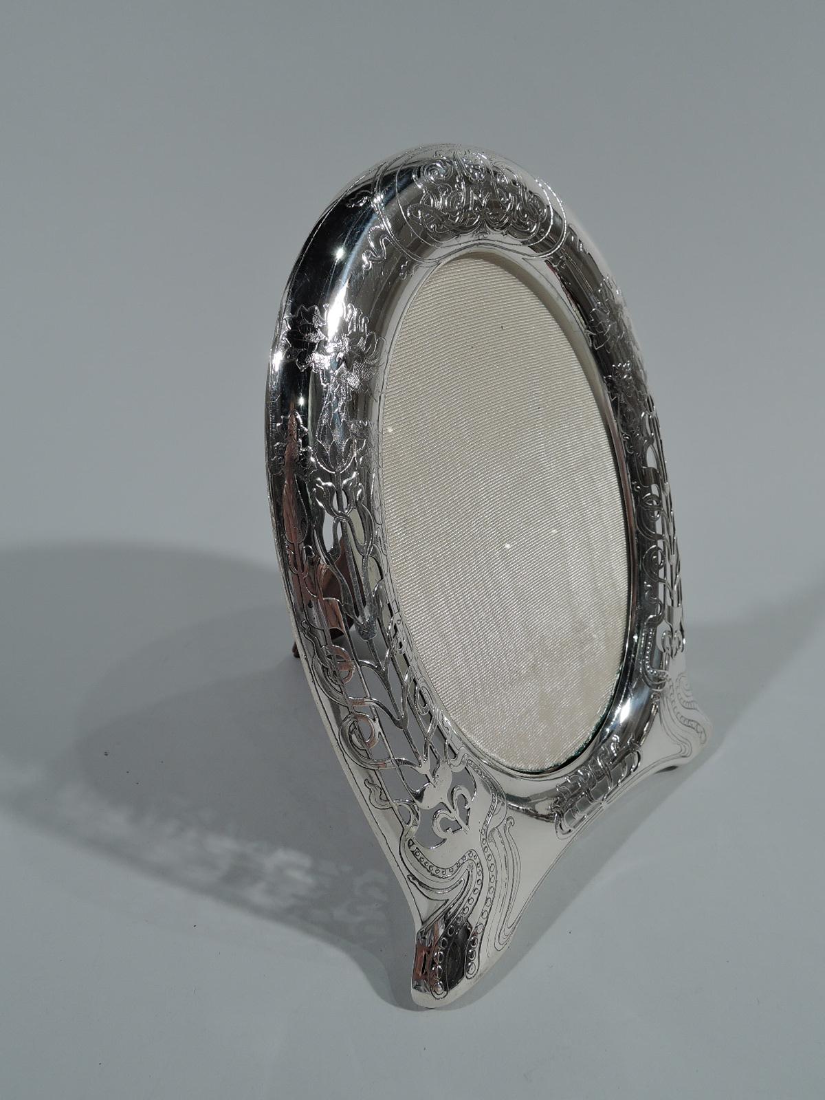 Art Nouveau sterling silver picture frame. Made by Tiffany & Co. in New York. Oval window in curved horseshoe-form surround with bracket feet. Semi-abstract fluid, sinuous flowers and interlaced tendrils. At top stylistically-integrated interlaced