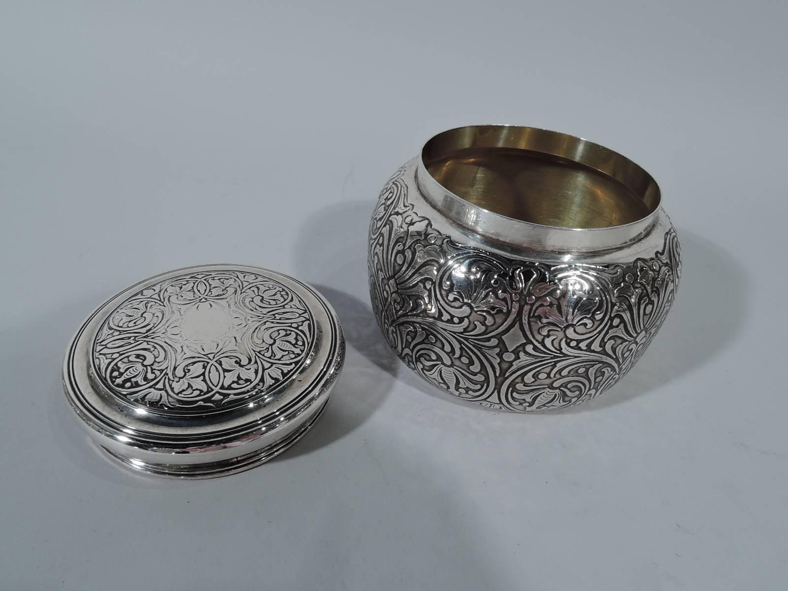 Art Nouveau sterling silver powder jar. Made by Tiffany in New York, circa 1908. Curved sides and snugly-fitted flat cover. Dense and stylized repeating scroll-and-flower design. Gilt-washed interior. A pretty period piece. Hallmark includes pattern